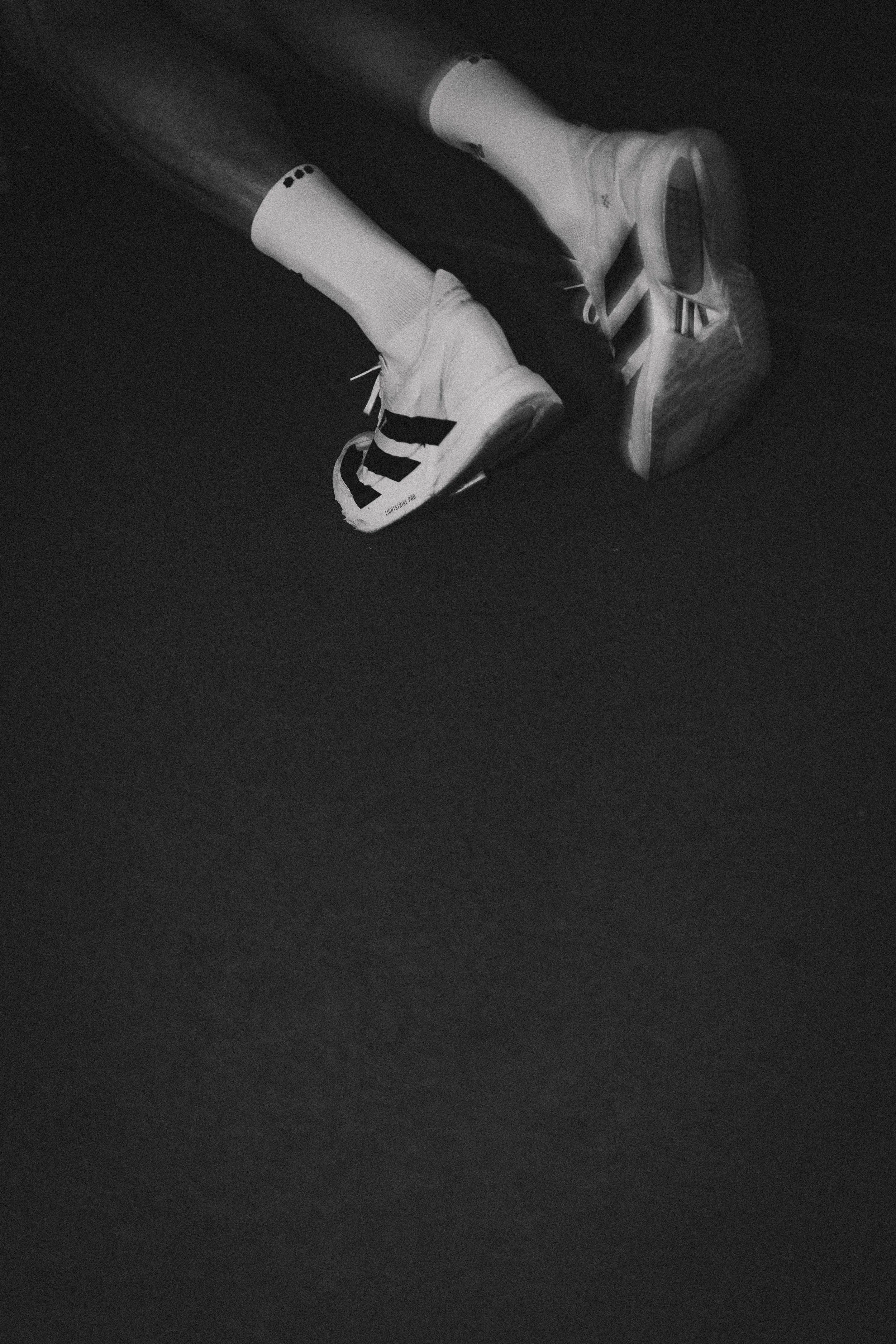 Pair of white athletic shoes with black accents, worn with white socks, lying on a dark surface.