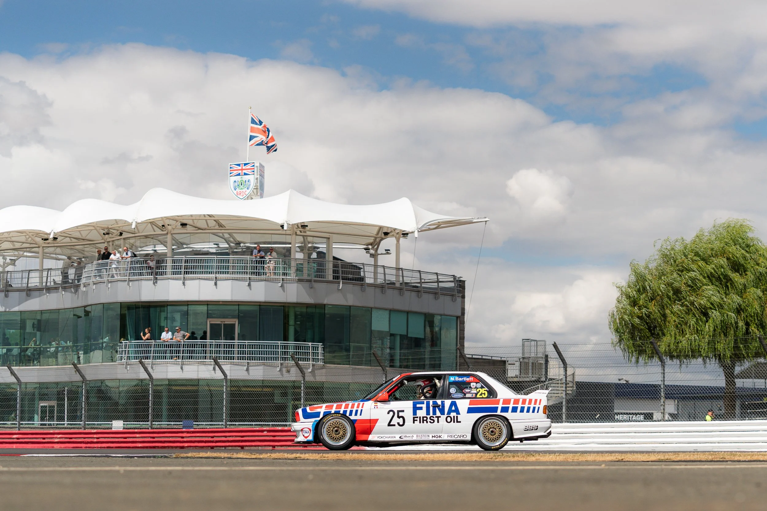 Race car on a track with a raceway building and spectators in the background.