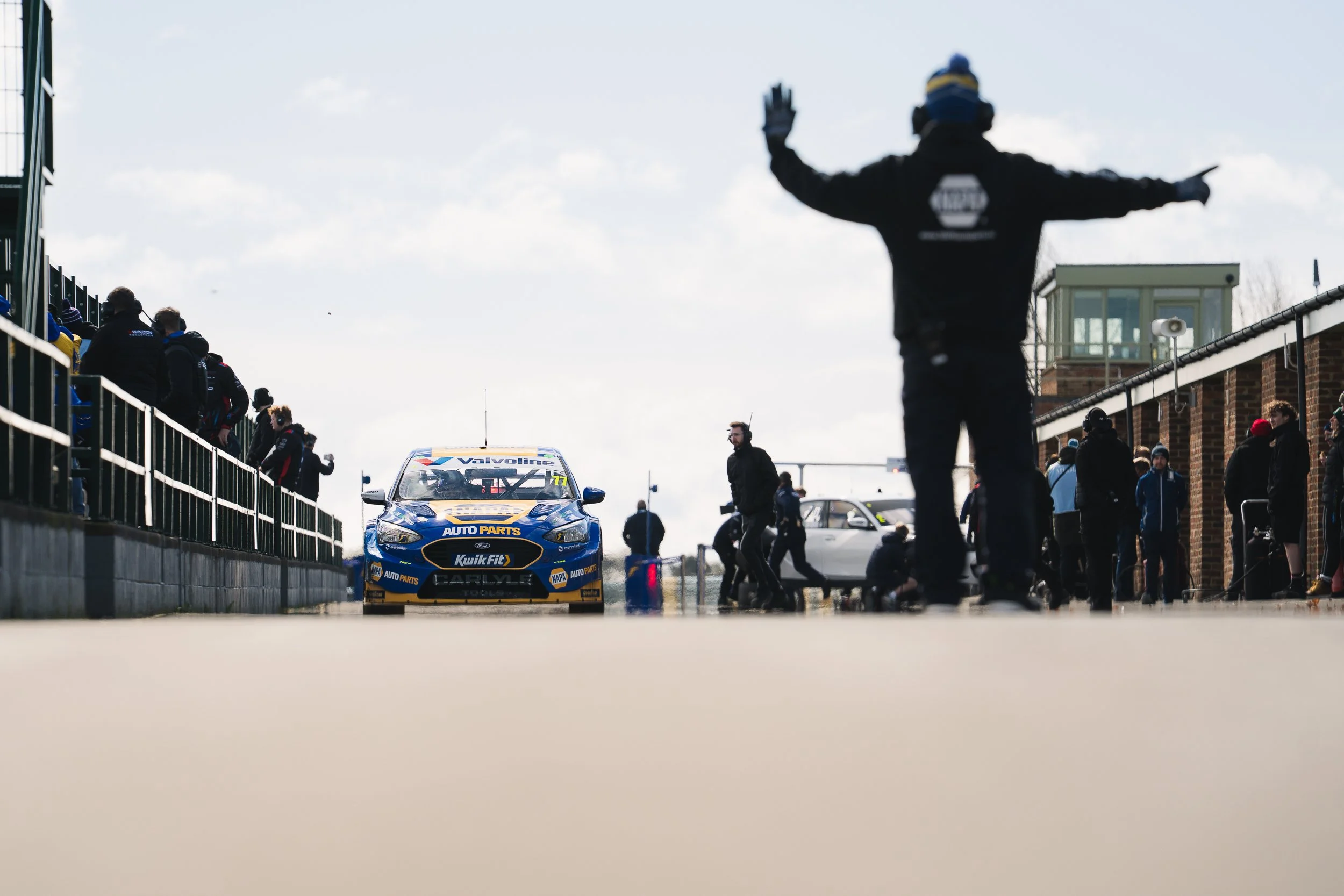 Marshal signaling a BTCC touring car out onto the wet pit lane at Croft testing