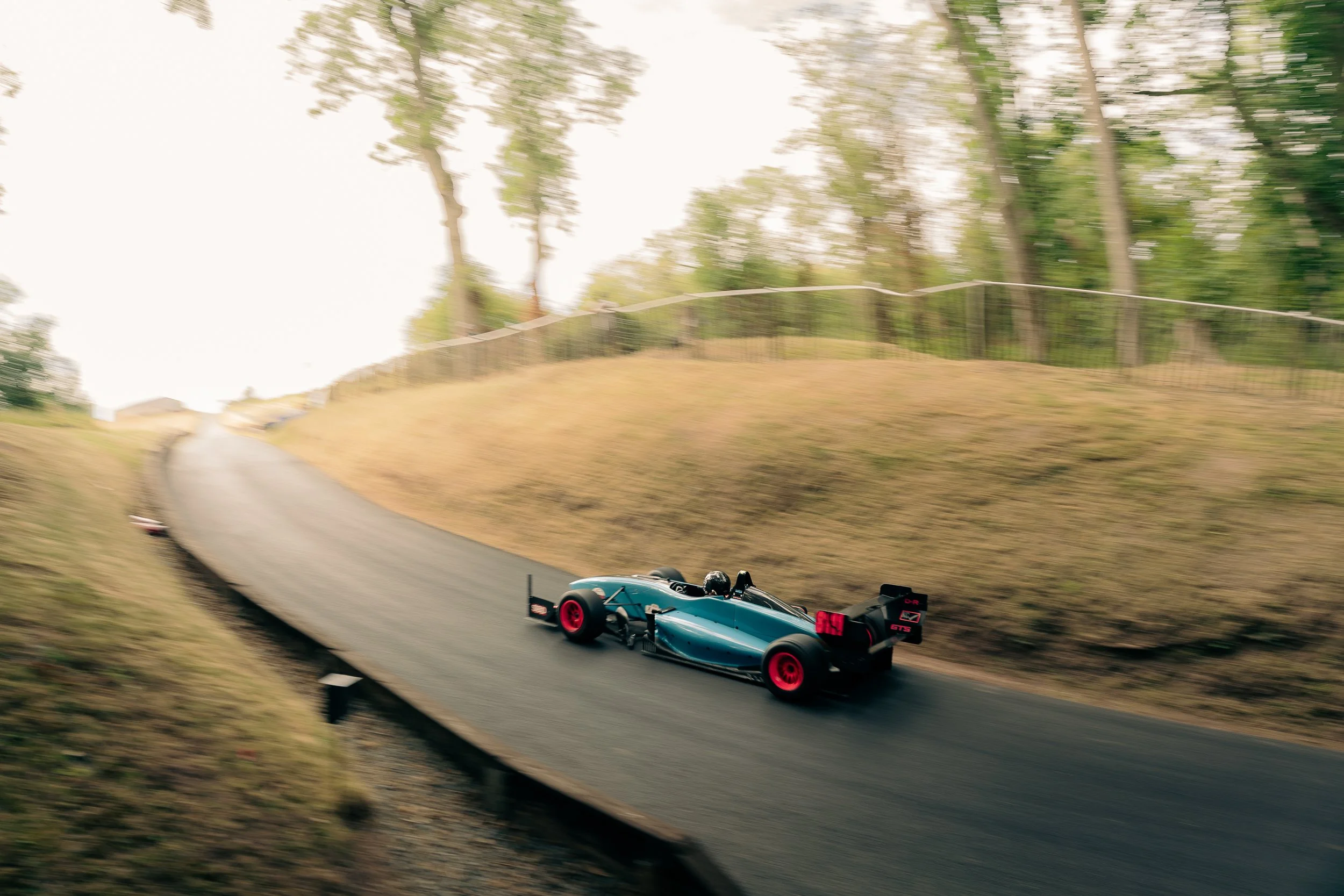 Teal single-seater racing car with motion blur powering through a tree-lined bend at Shelsley Walsh Championship Challenge