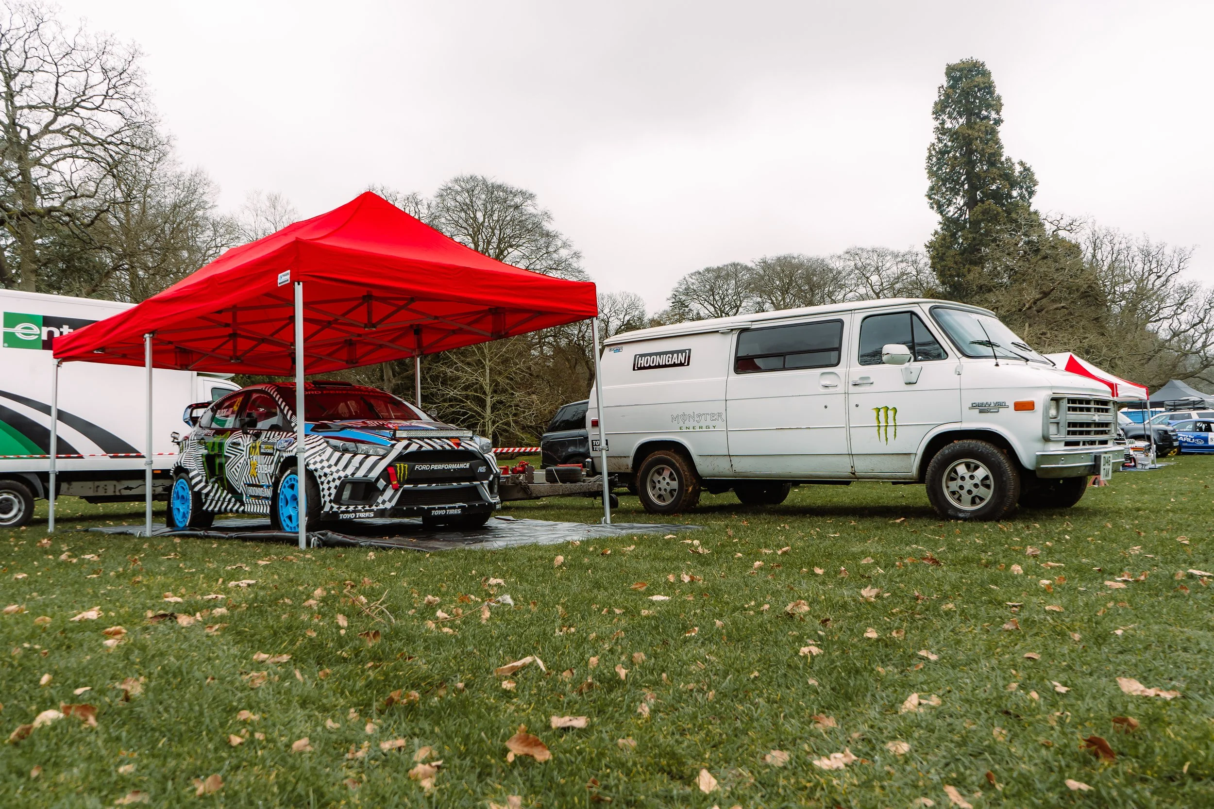 Hoonigan-liveried rally car parked under a gazebo beside the team van at the Lombard Rally Festival