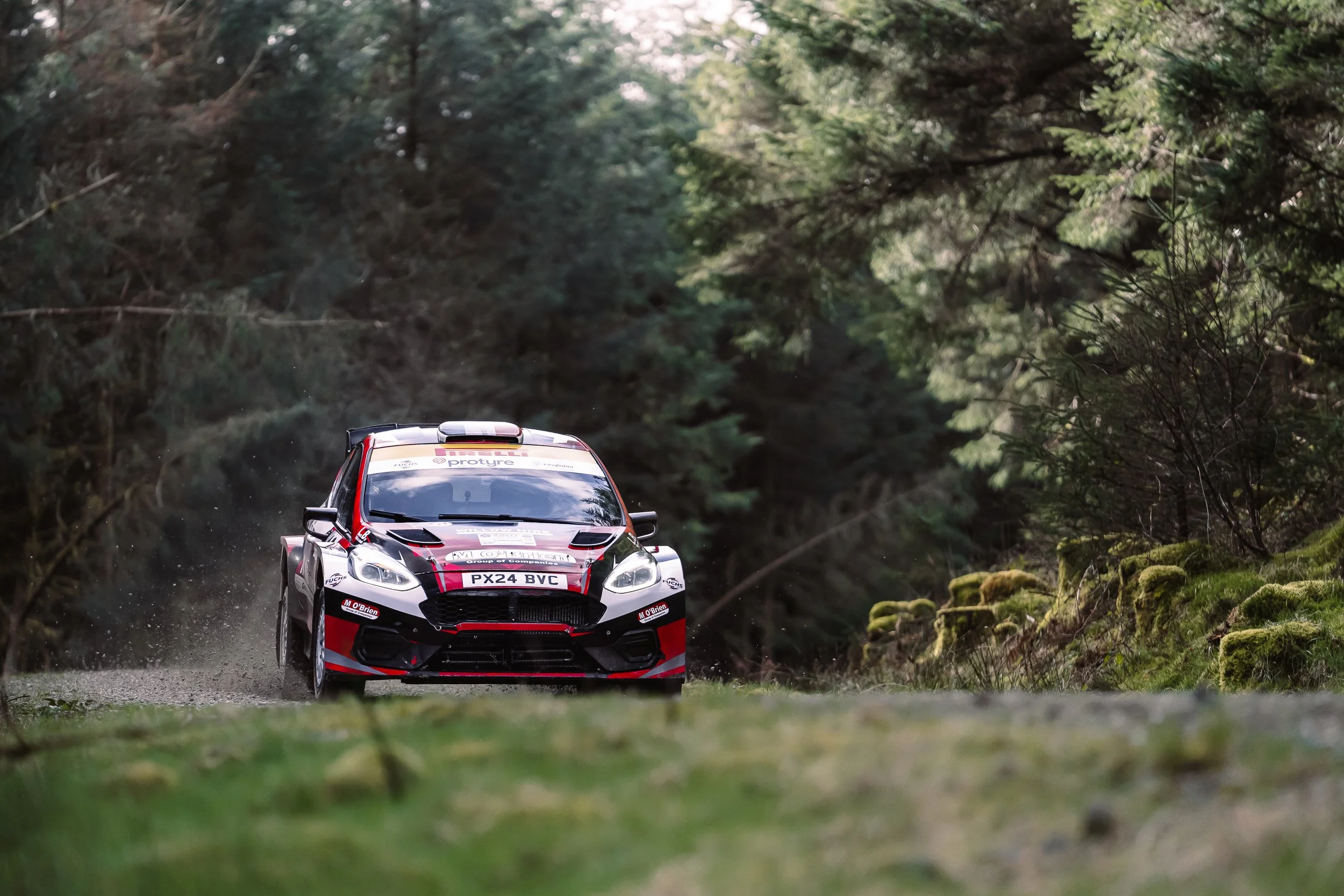 Red and white rally car cornering on a gravel forest stage at Rally North Wales