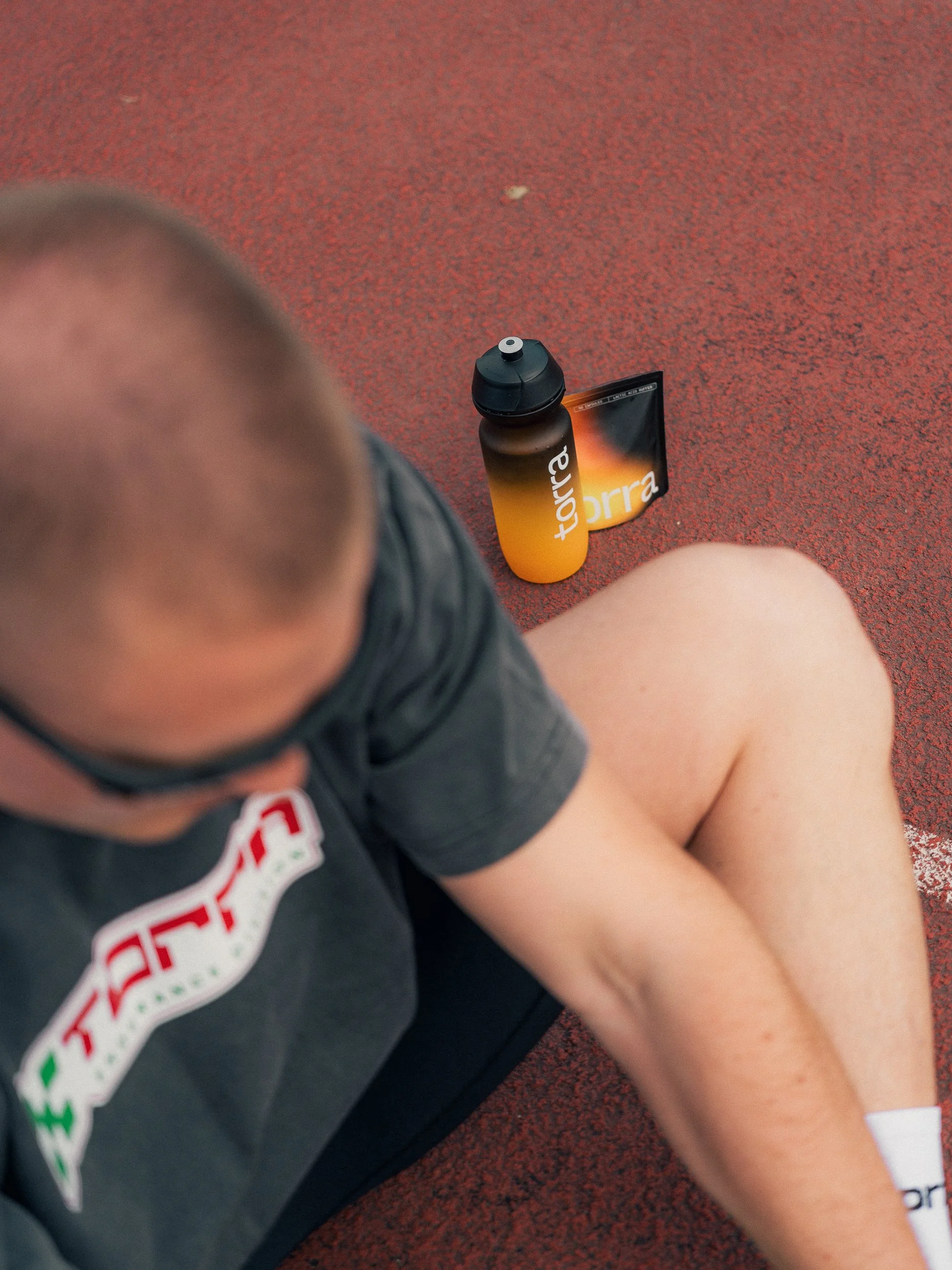 Overhead shot of an athlete resting on the track with a Torra drink bottle, Torra Performance Mens Health campaign