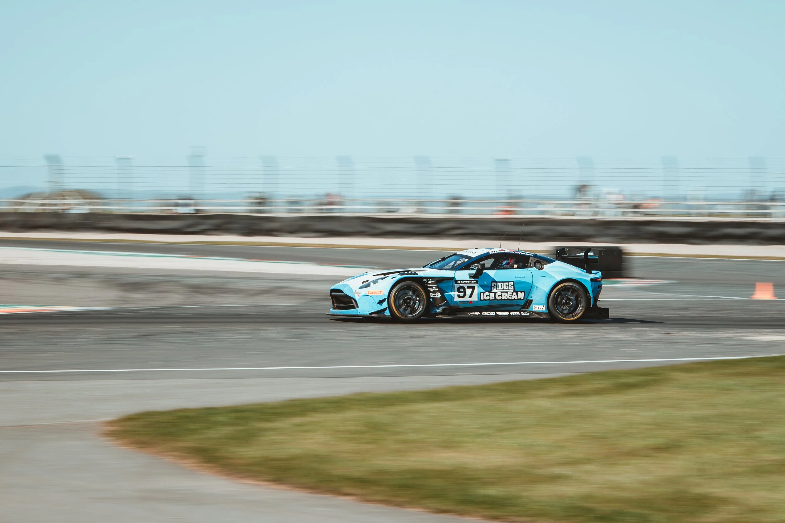 A blue race car with the number 97 and sponsor logos driving on a race track.