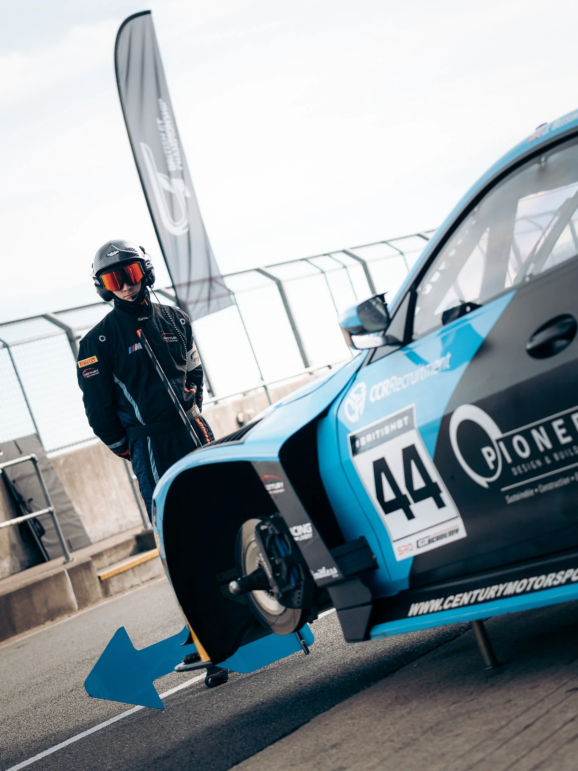British GT driver standing beside a blue Aston Martin GT3 car in the pit lane at Silverstone 500