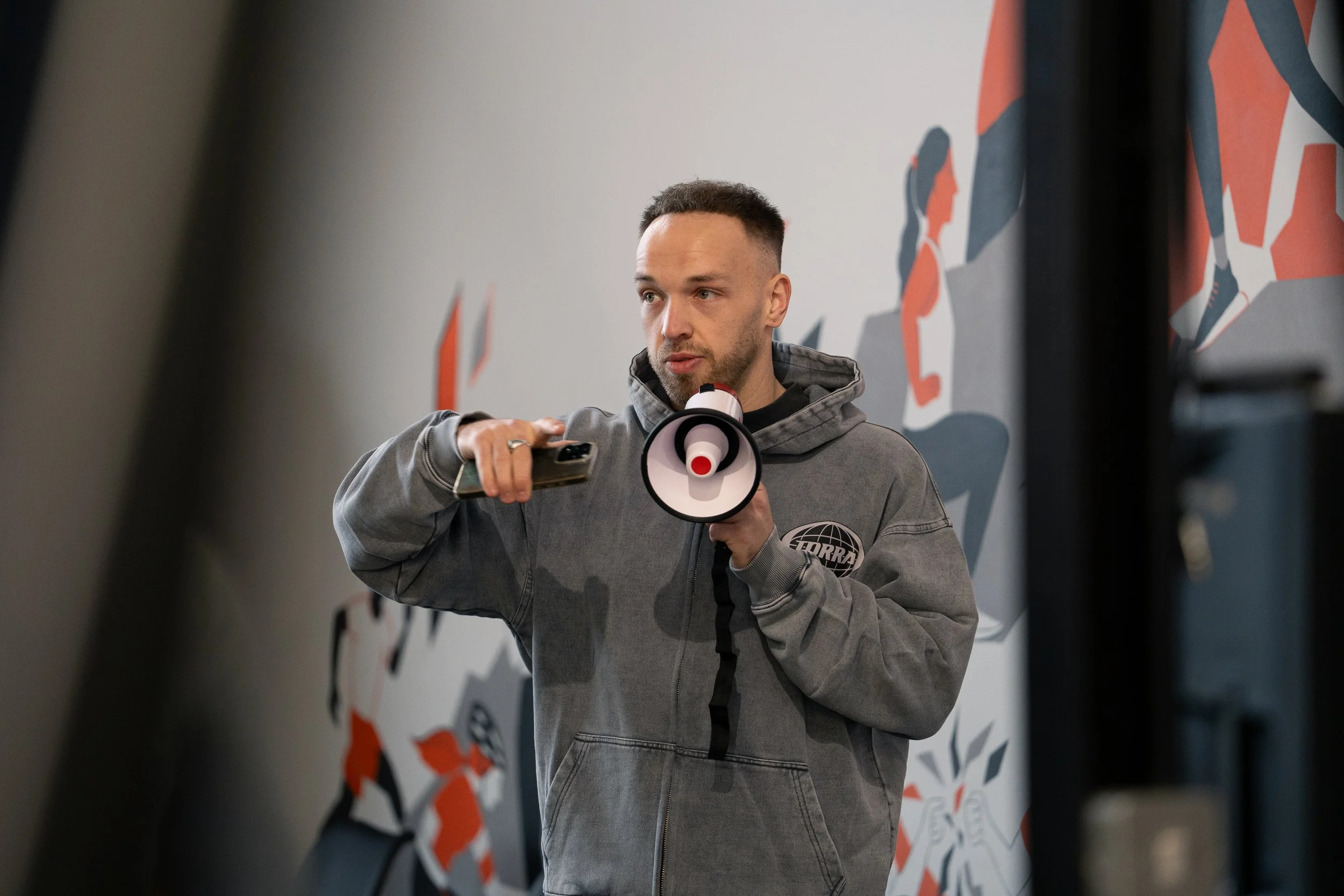 Man in a Torra hoodie speaking through a megaphone against a mural backdrop for the Engine Series campaign