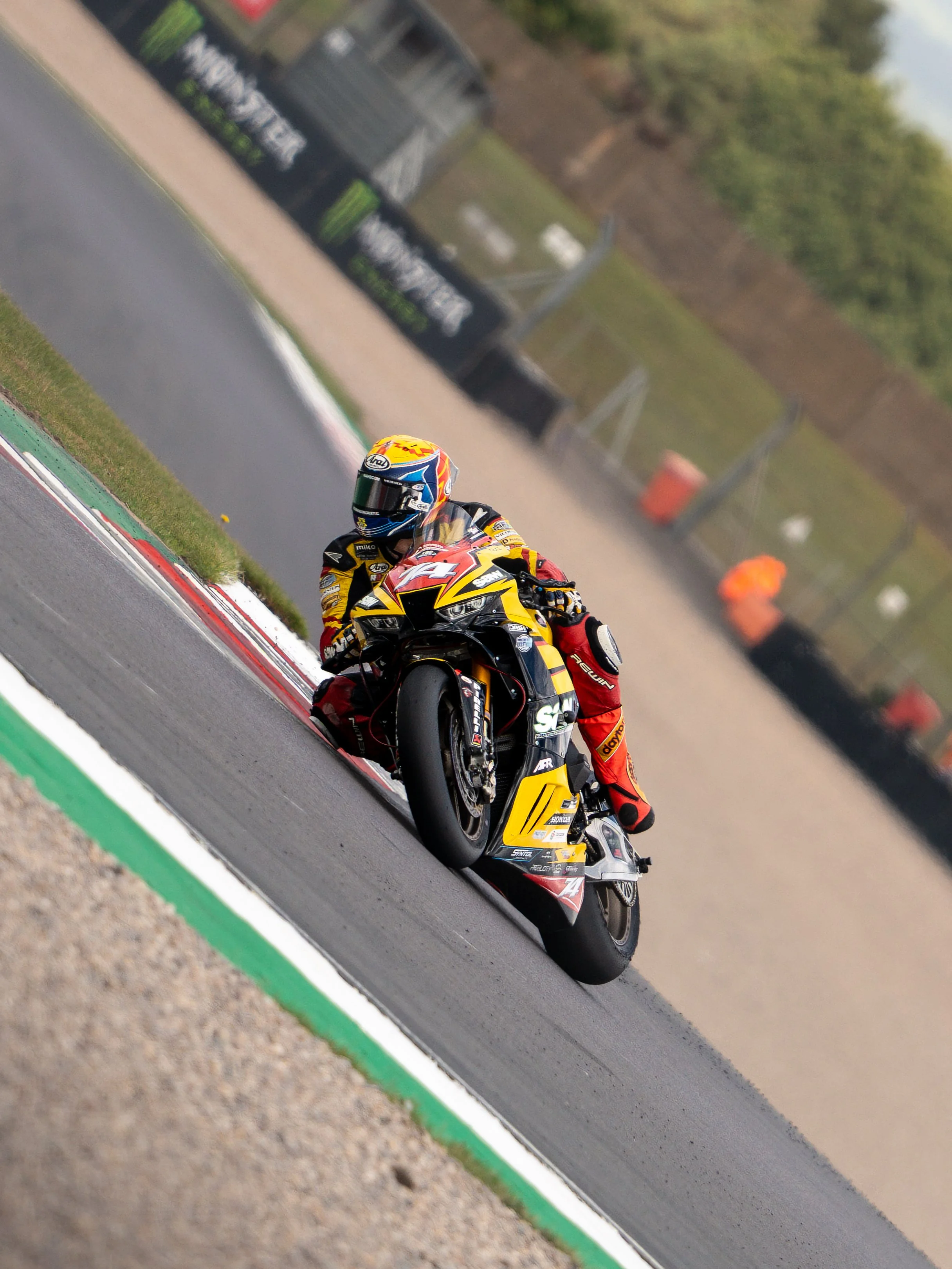A motorcycle racer in a yellow, black, and red suit leaning into a turn on a race track.