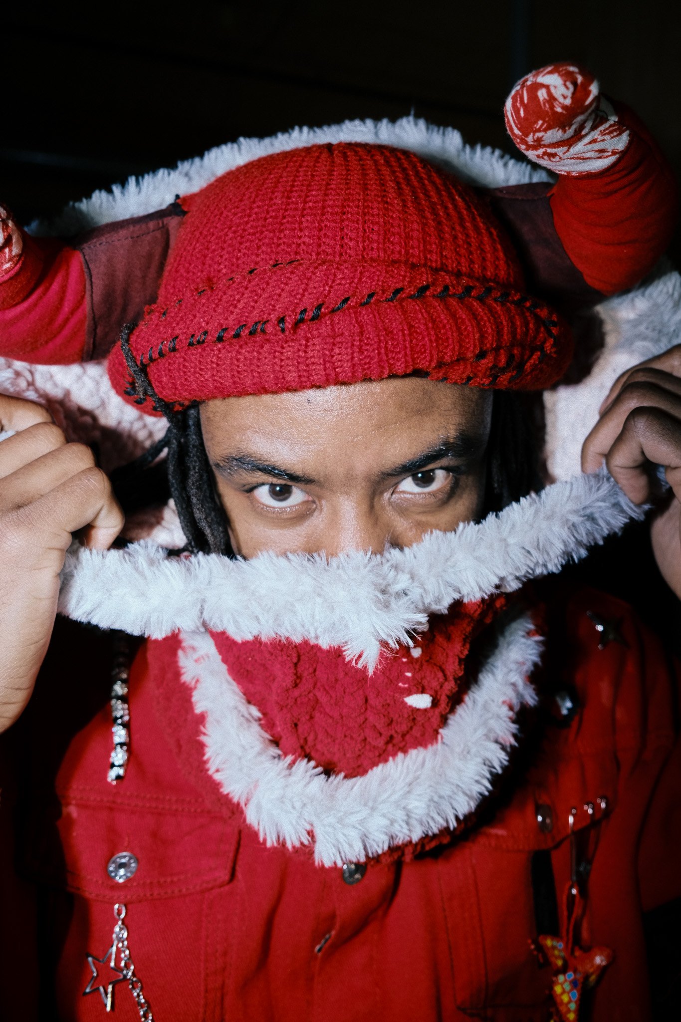 A person dressed in a red festive holiday costume with a hat and scarf, peeking over the edge of a fluffy white trim.