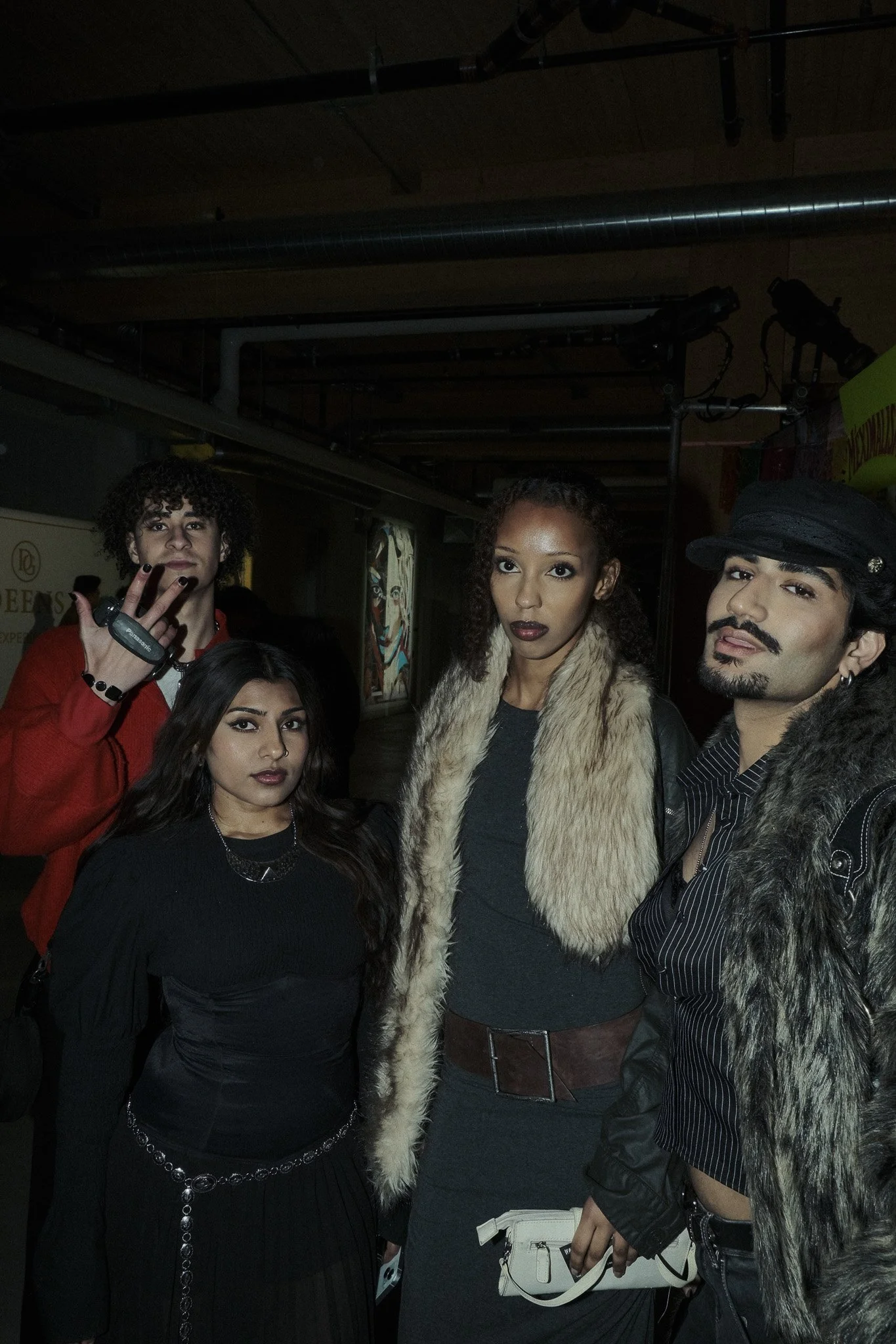 Group of four young adults in dark clothing posing indoors at night