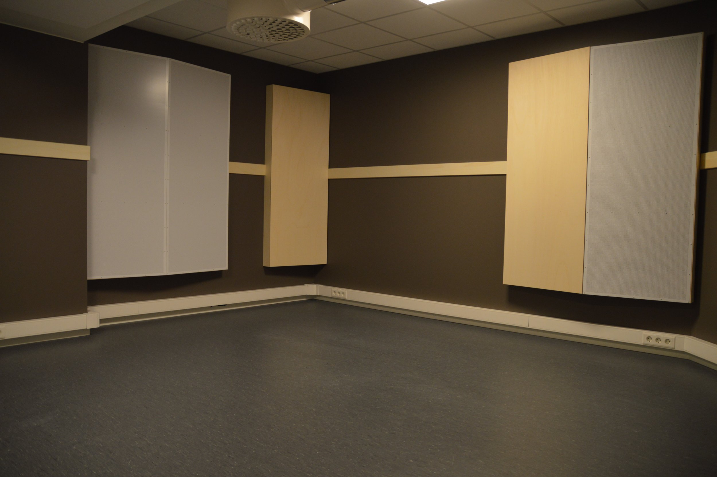 Tomt rom med brune vegger, to hvite og to beige veggskap, svart teppe og elektriske uttak langs gulvet.