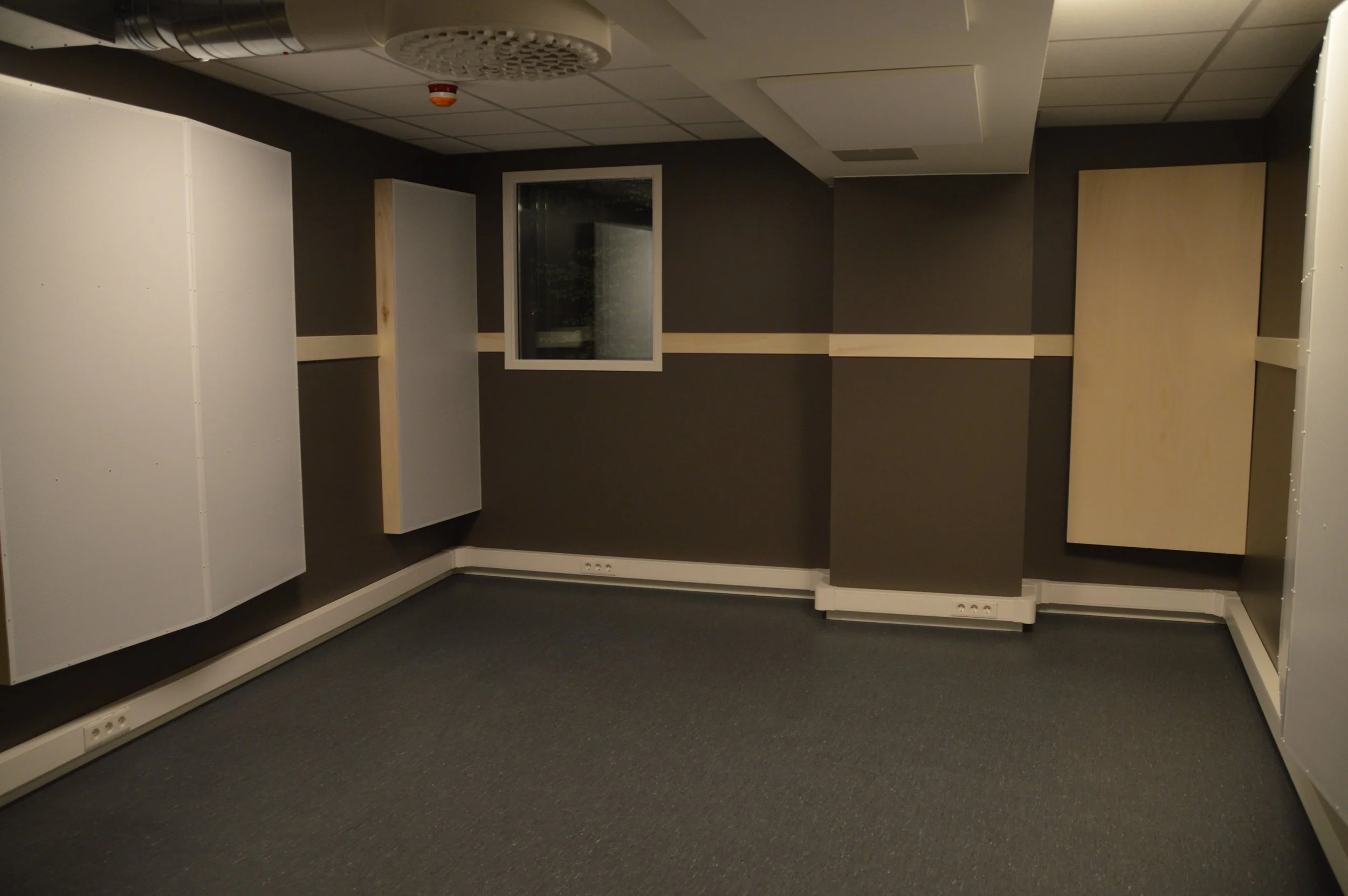 Et tomt kontorlokale med grå vegger, gulvteppet og noen hvite paneler på veggene.