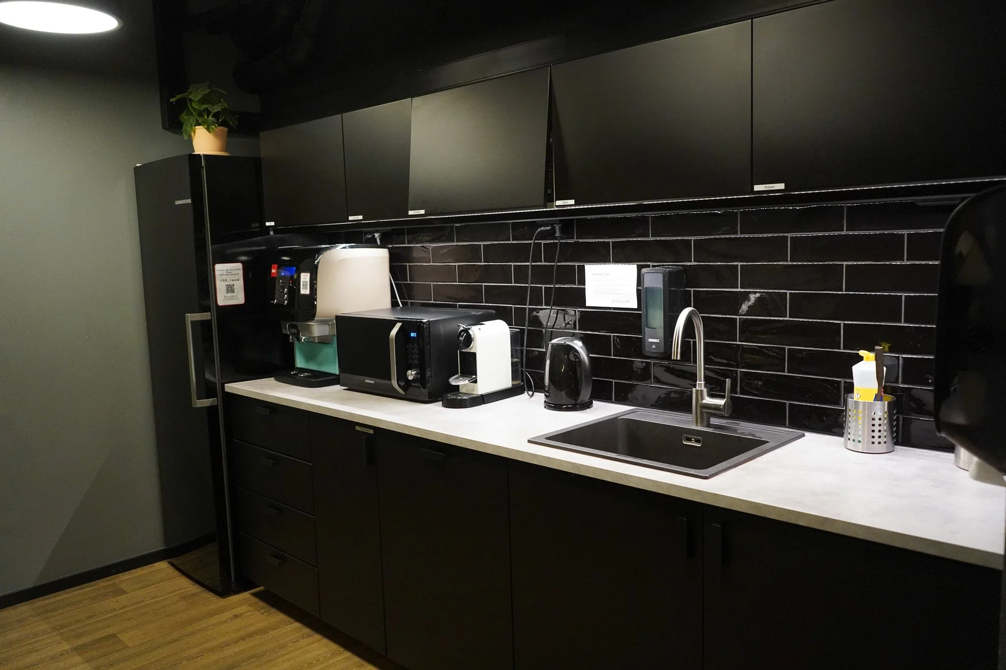 Kjøkkenskap, mikroovn, vannkoker, oppvaskkumm, oppvaskmiddel, og annet kjøkkenutstyr på en kjøkkenbenk.