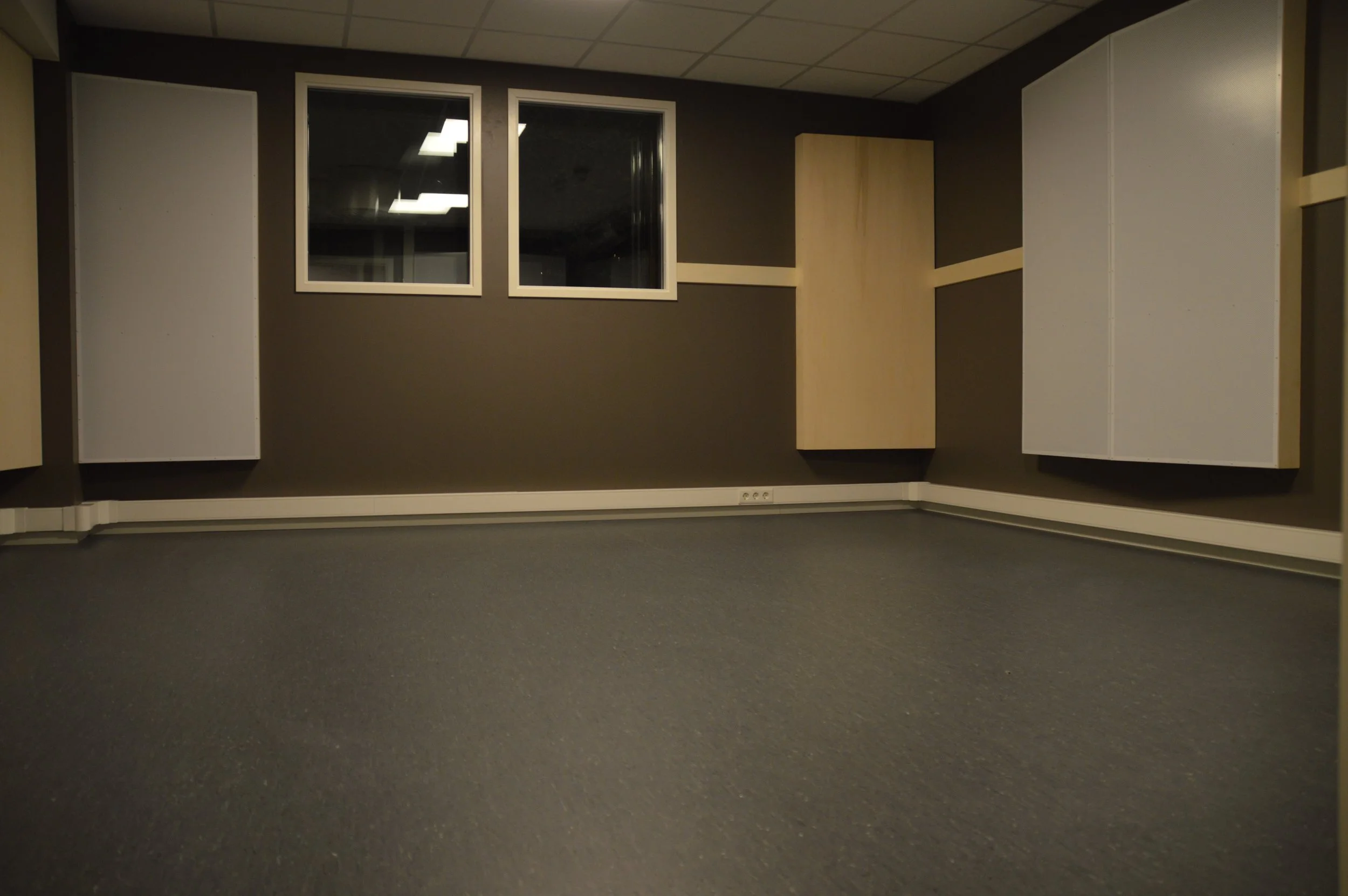 Et tomt rom med mørkegrå vegger, mørk grå teppe og noen hvite og lette tre paneler på veggene.