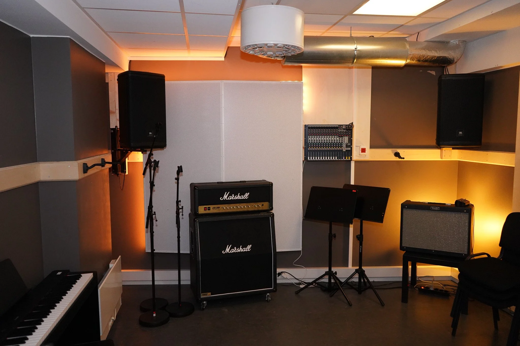 Musikklokale med gitarforsterker, piano, mikrofoner, høyttalere og lydutstyr.