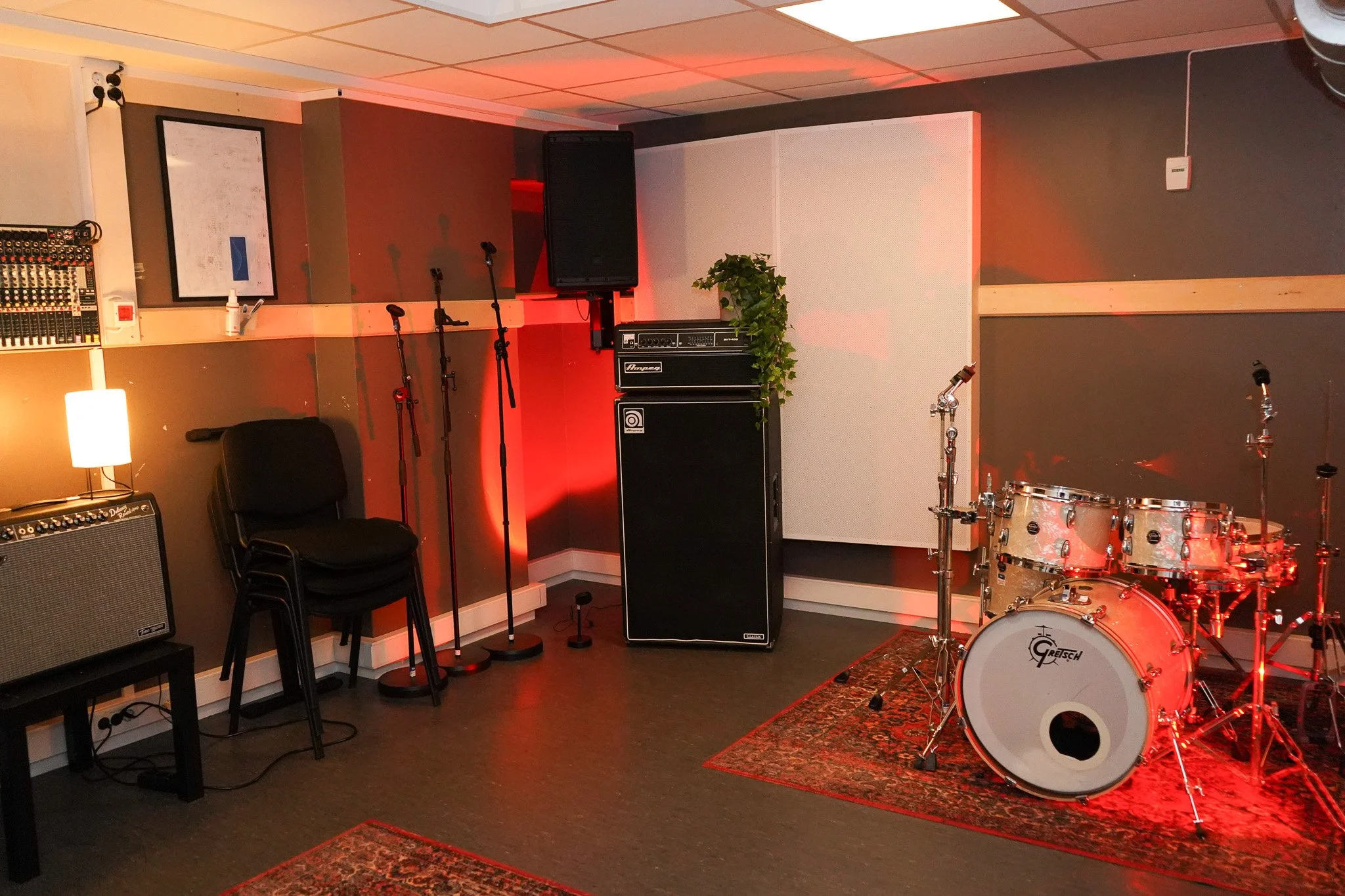 En musikkøvelsesrom med trommesett, forsterker, mikrofonstativer og lydutstyr.
