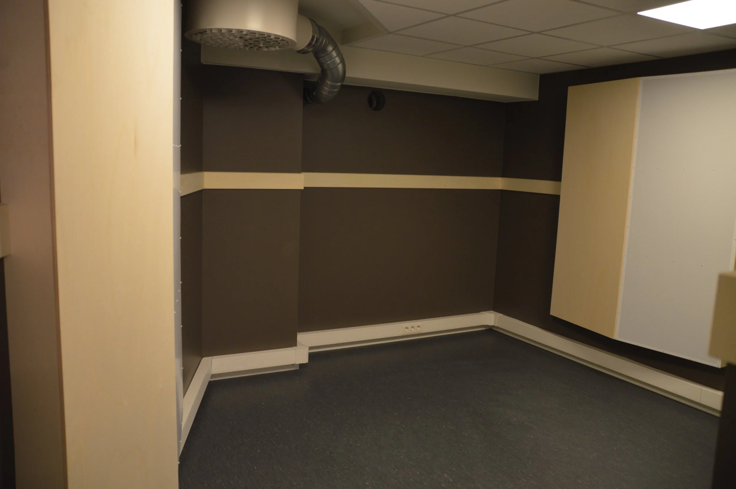 Tomt, liten blokkering med mørke vegger og gulv, ventilasjonsrør i taket.