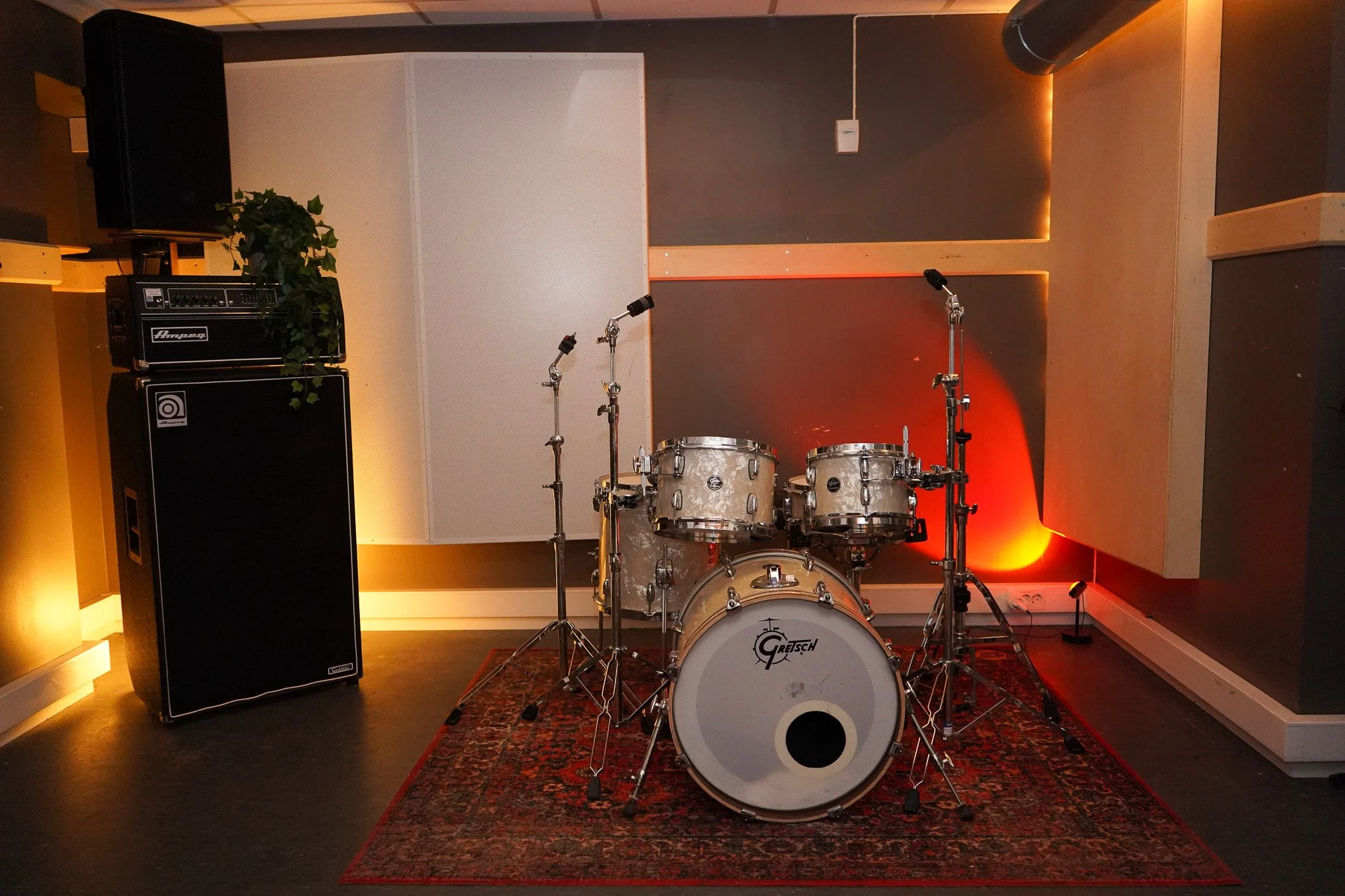 En trommesett på en teppe i et rom med lydisolering. Tre mikrofonstativer står rundt trommesettet.