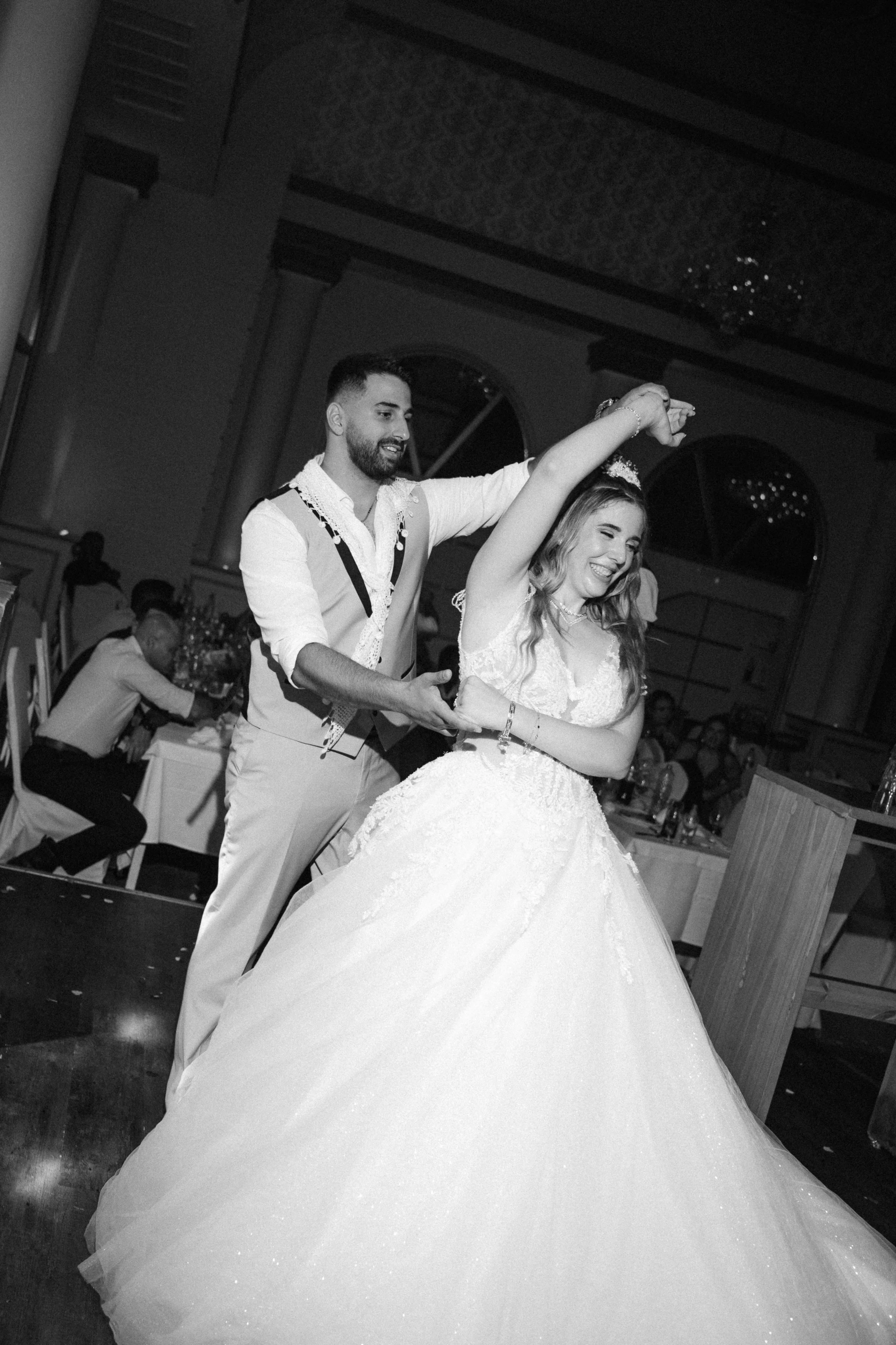 A black-and-white photo of a wedding dance, showing a groom twirling the bride in a ballroom setting.