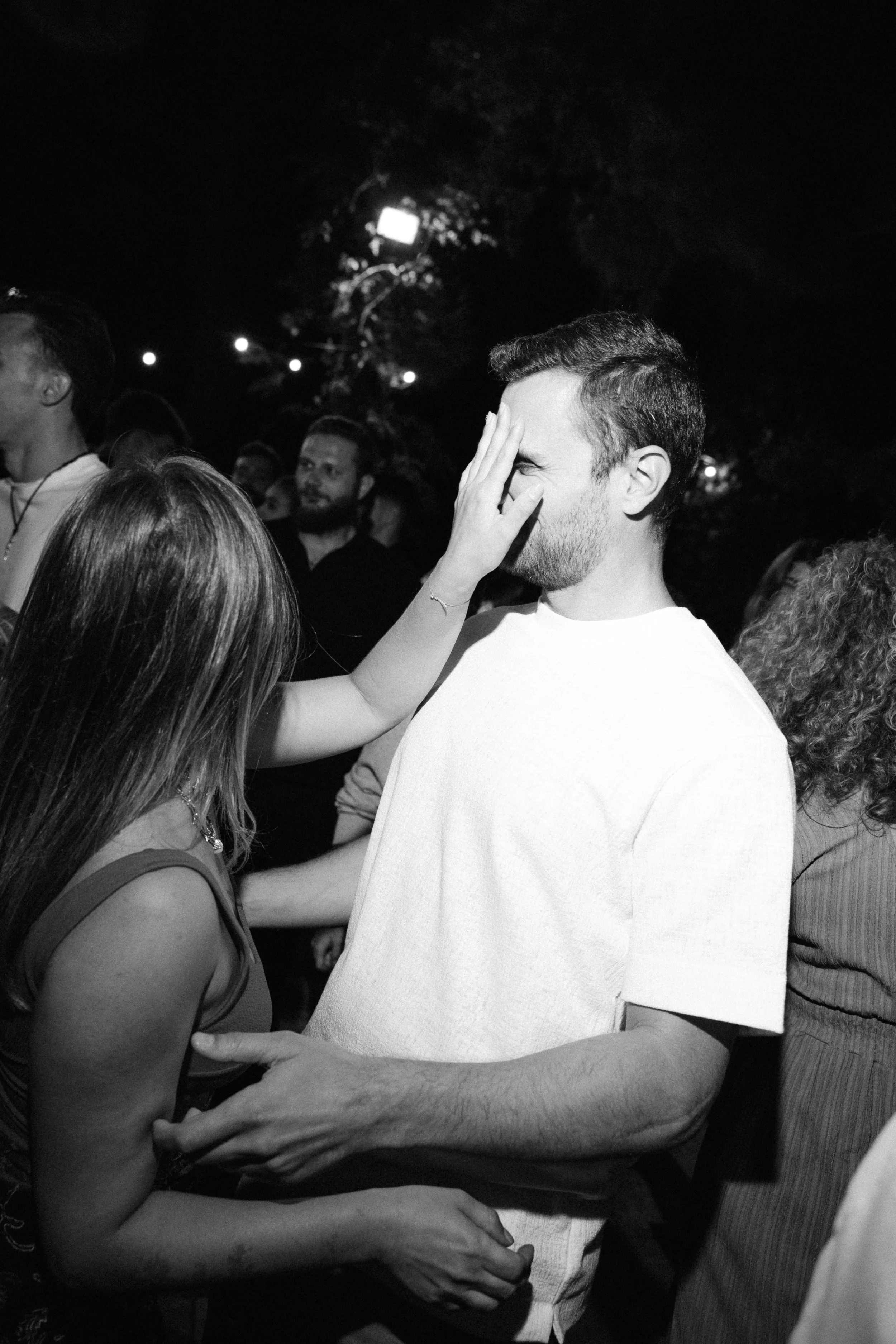 A woman playfully touching a man's face at an outdoor event at night.