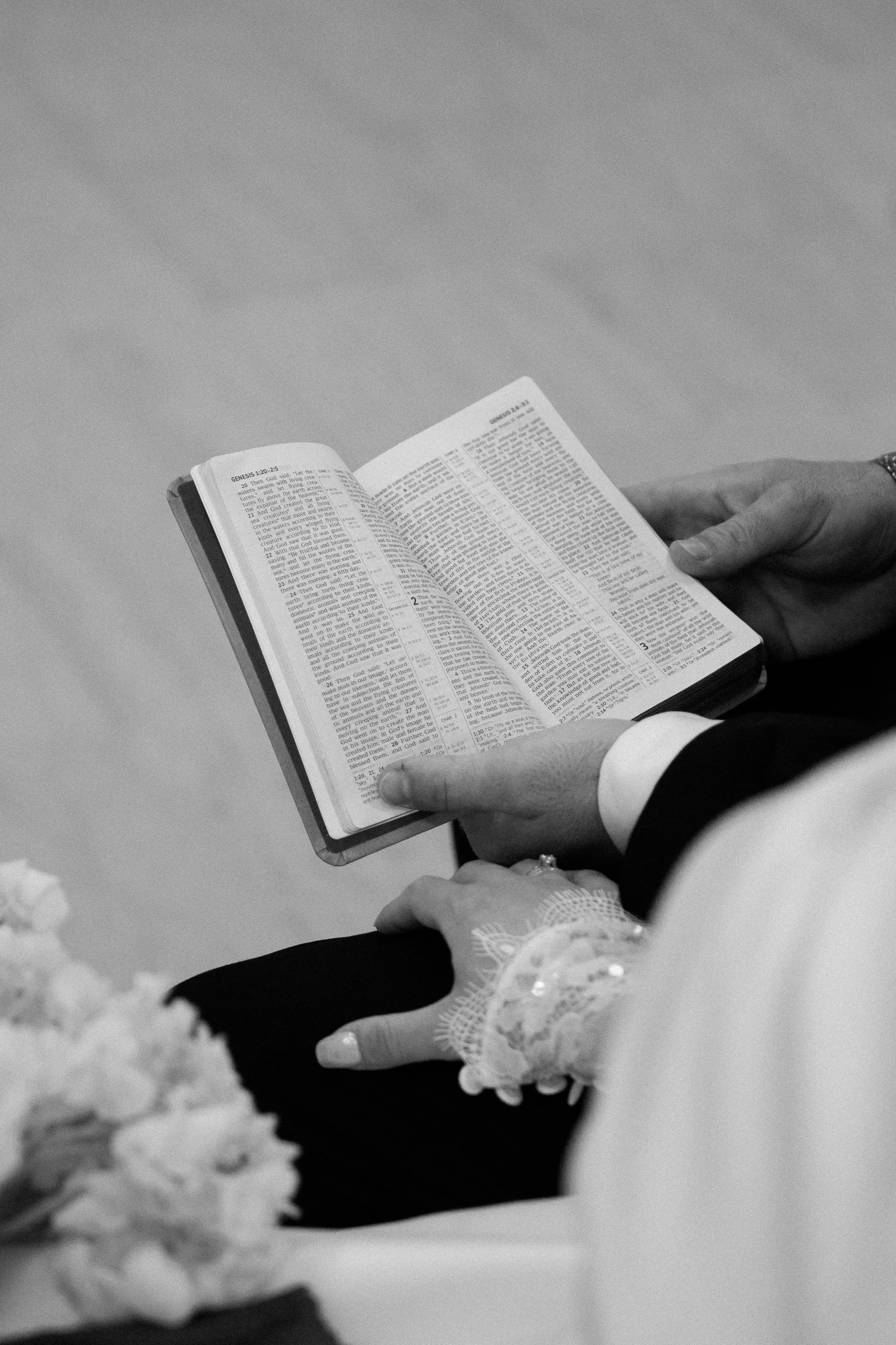 A person holding a Bible and reading it, seen from above in black and white.
