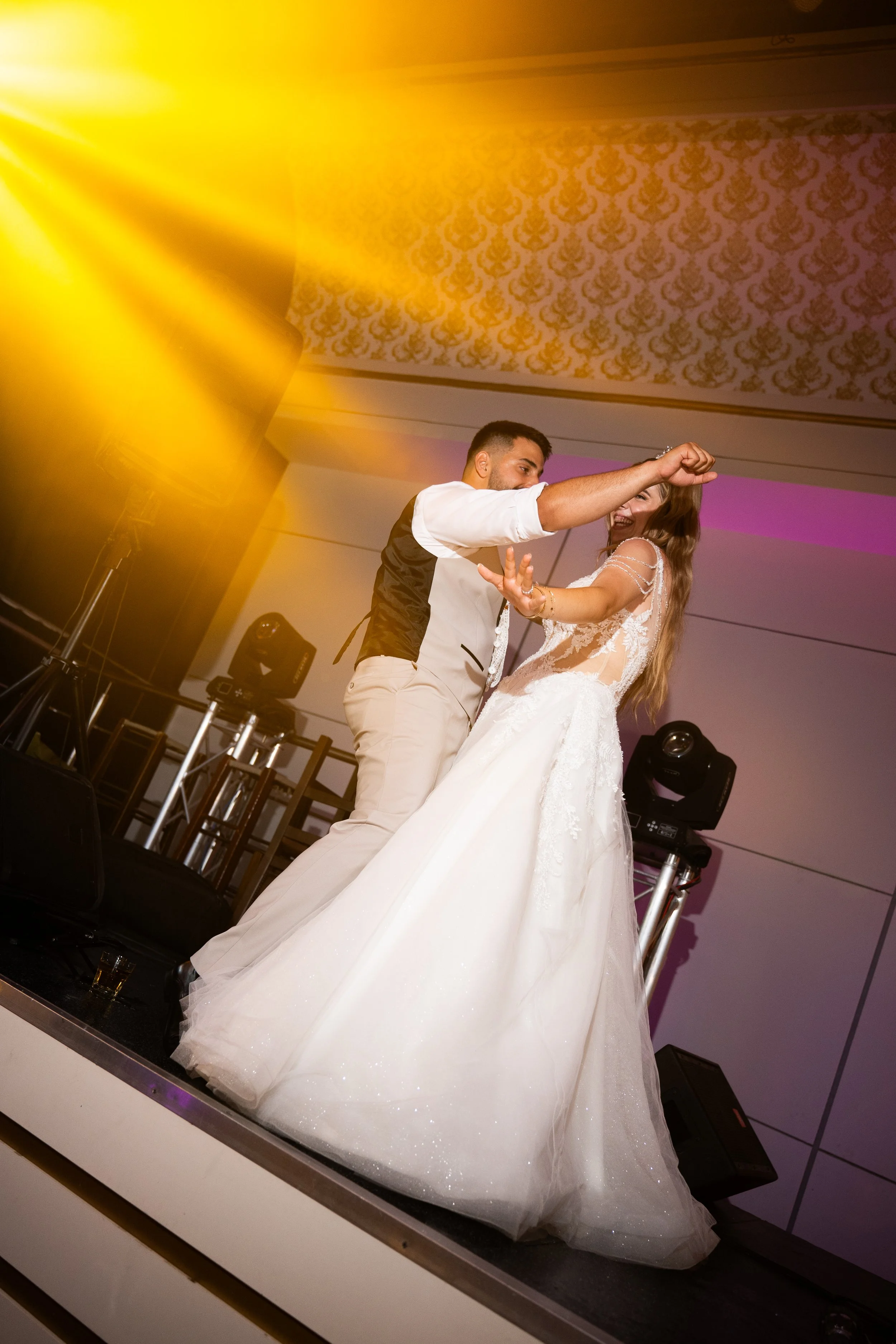 A bride and groom dancing at their wedding reception, with colorful lighting and dance floor in the background.