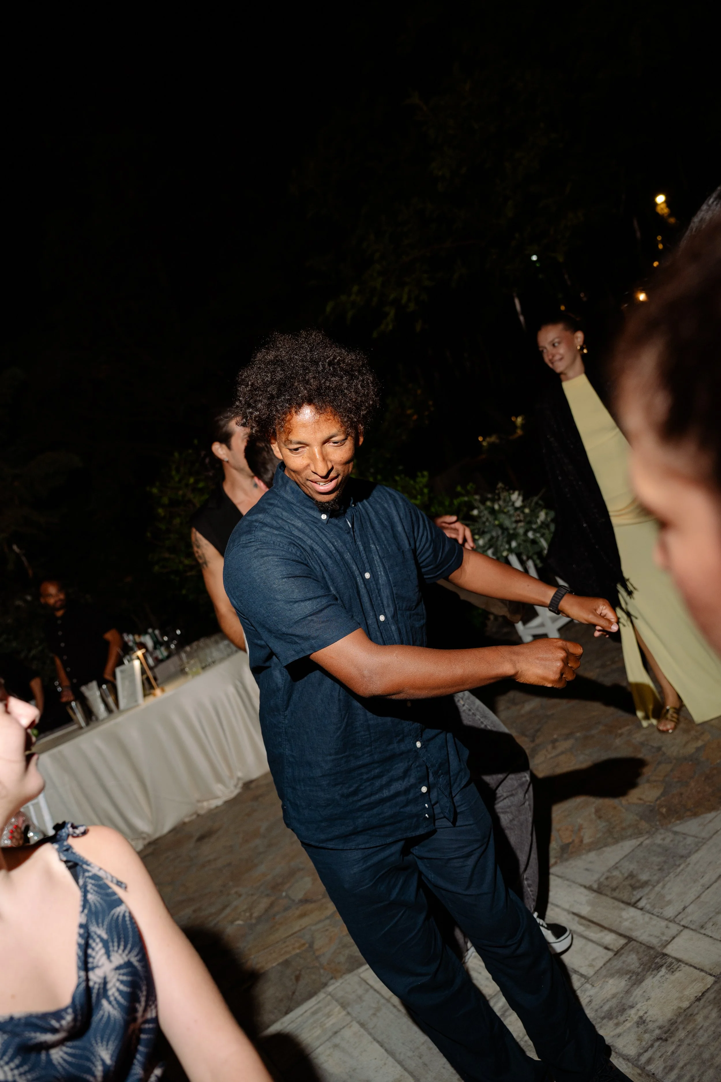People dancing at an outdoor event during the night, with a table of drinks in the background.