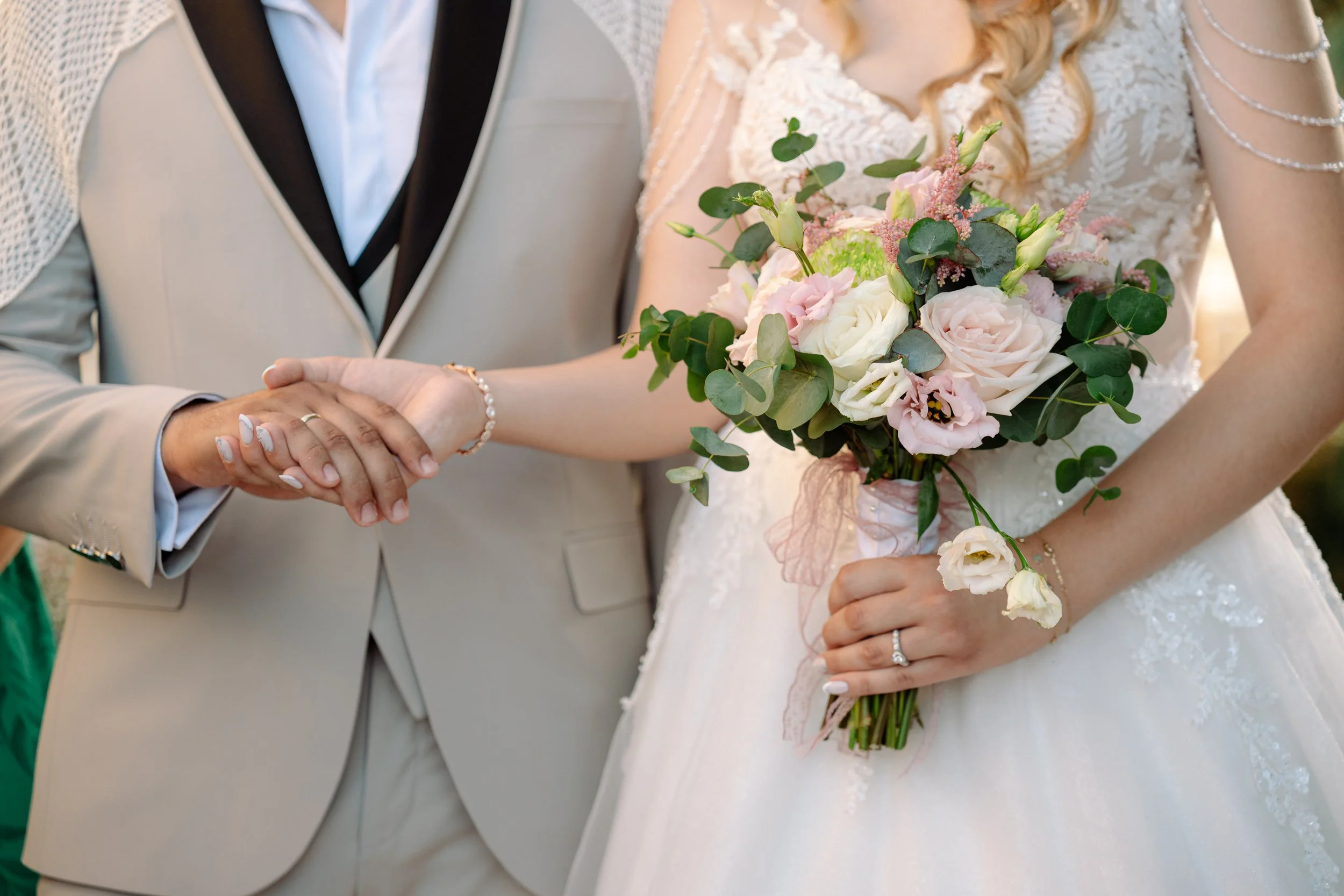 A bride holding a bouquet of pink and white flowers and an officiant or another person holding her hand, at a wedding ceremony.