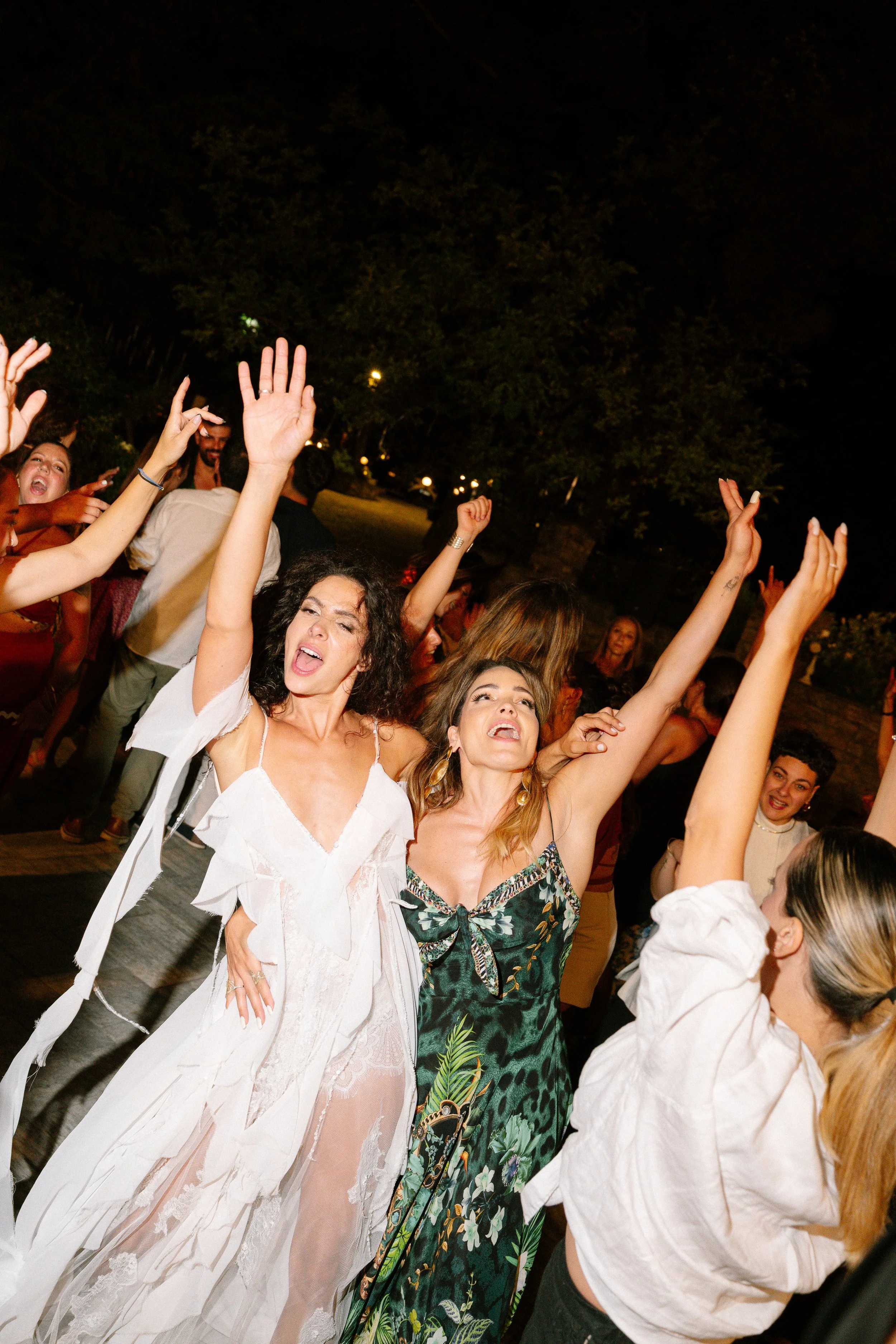 People dancing and celebrating outdoors at night with their hands raised, enjoying a lively event.