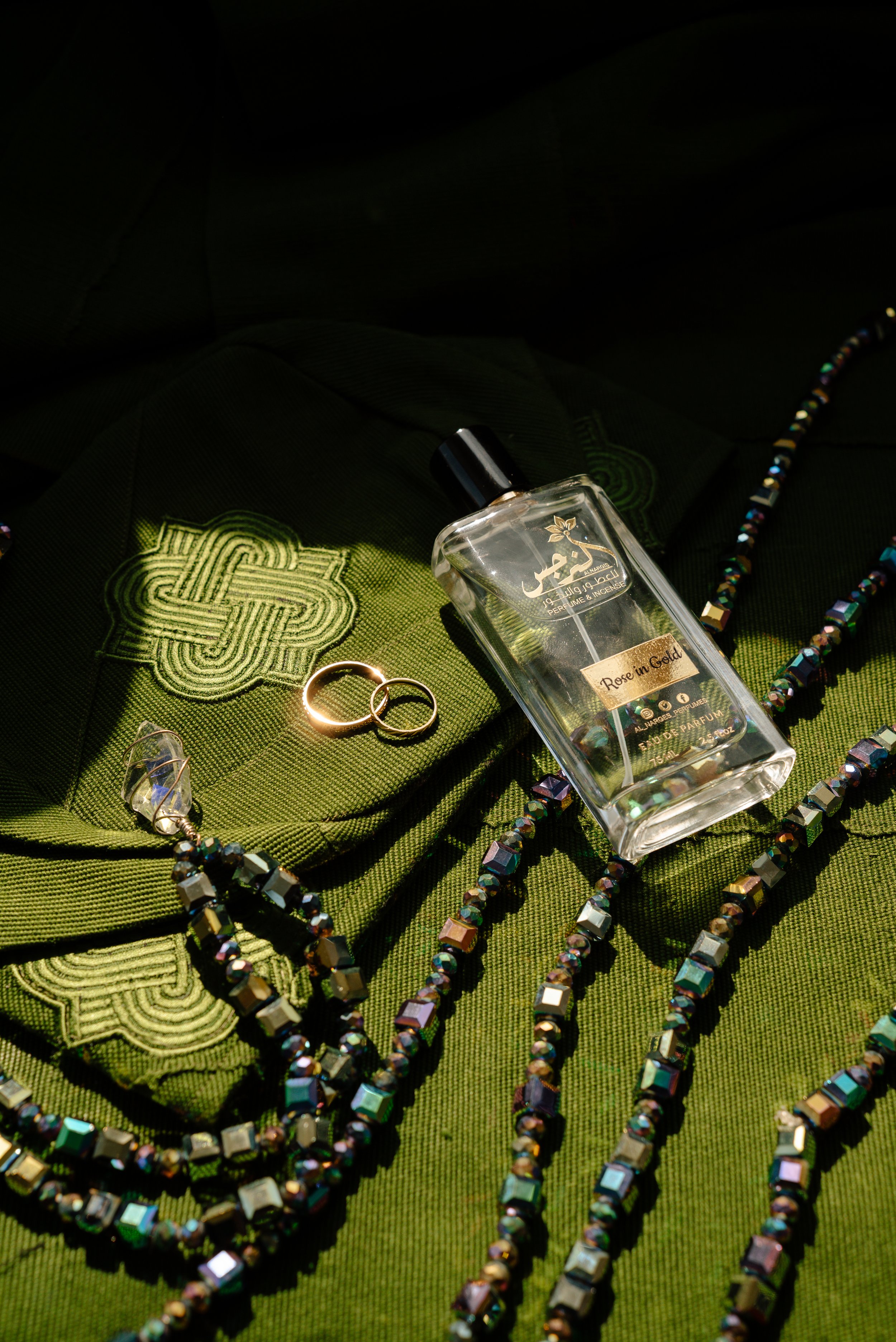 Jewelry, perfume, and rings on a green fabric background illuminated by sunlight.