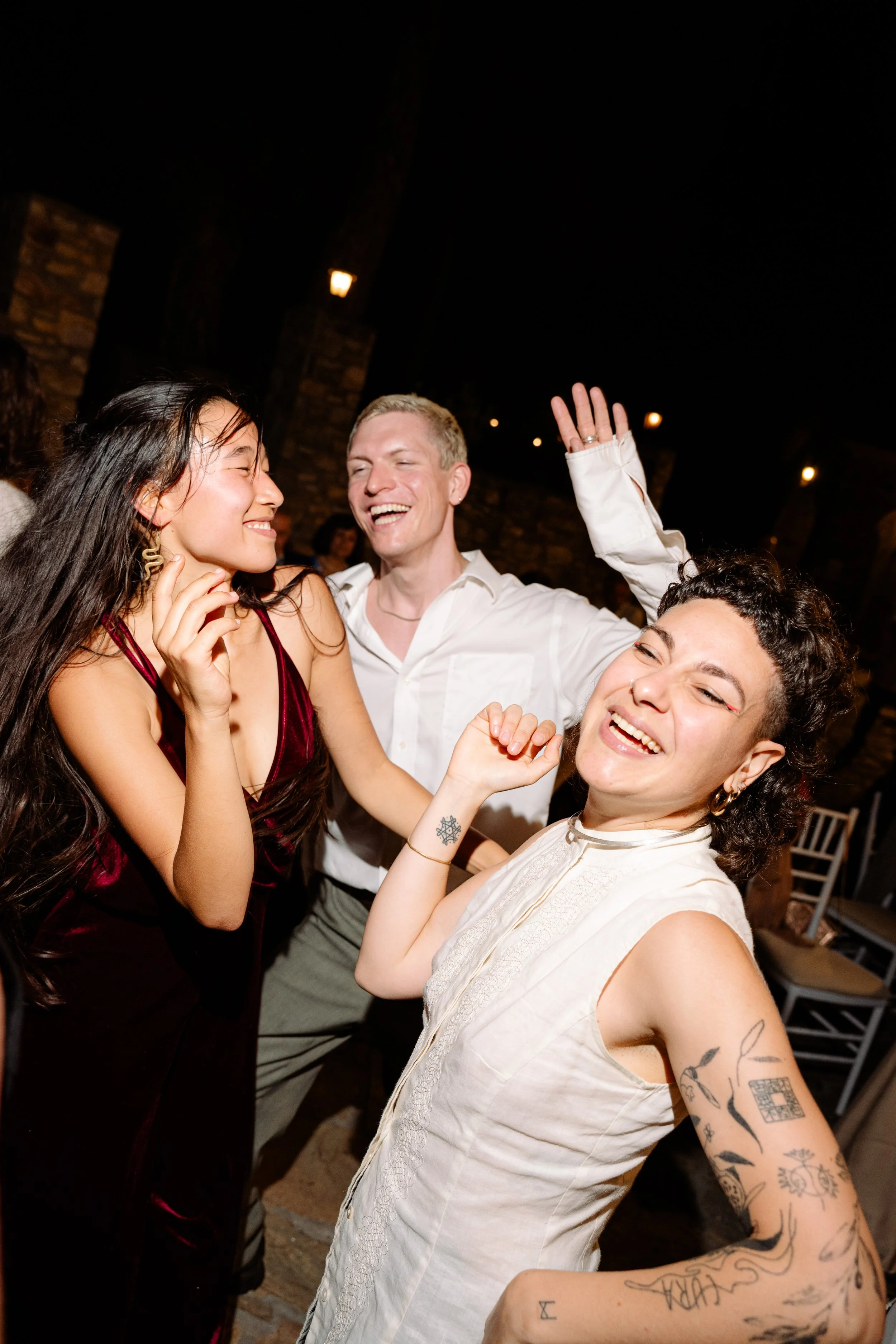 Group of friends dancing and laughing at a night event, celebrating outdoors with warm lighting and casual elegance.