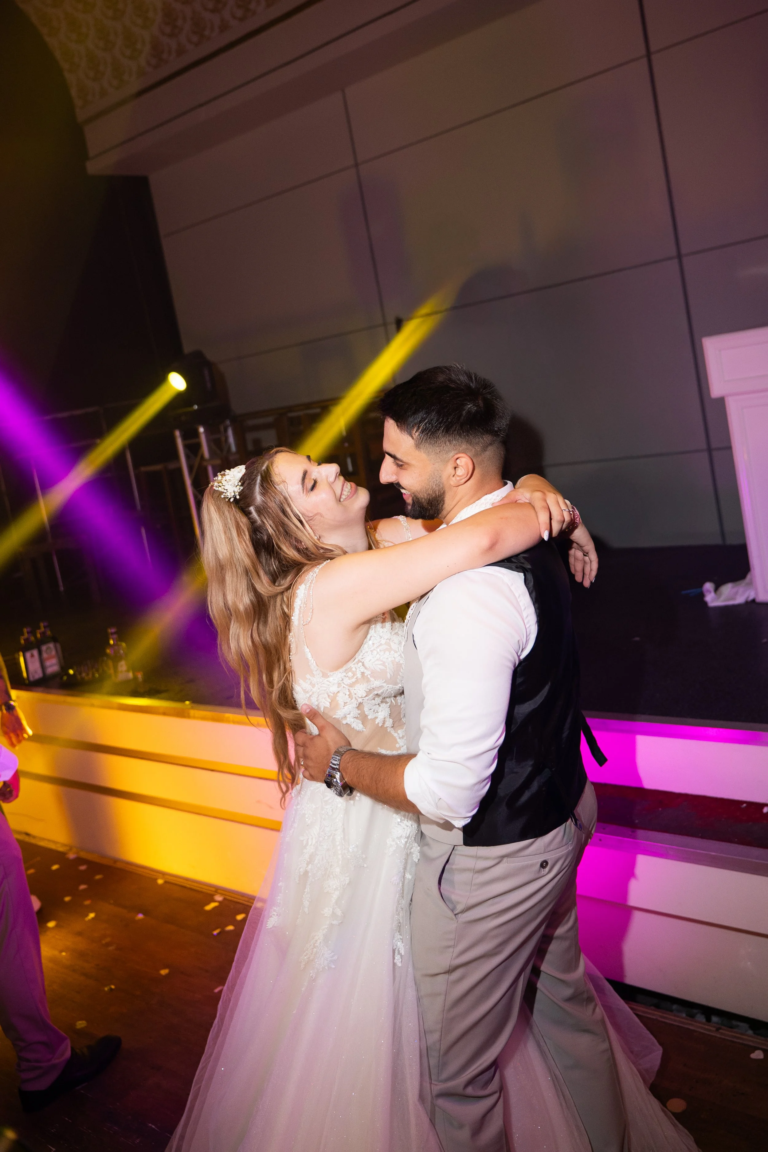 A bride and groom dancing and embracing at their wedding reception with colorful party lights.