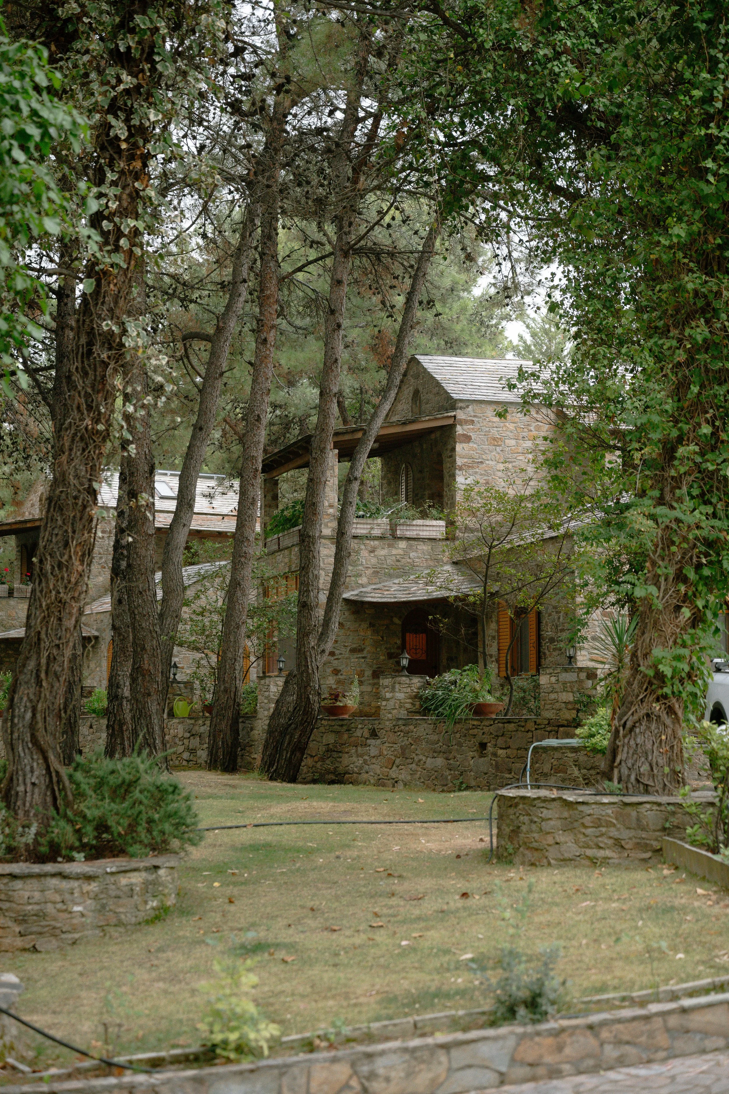 A stone house in a wooded yard with trees and a small lawn.