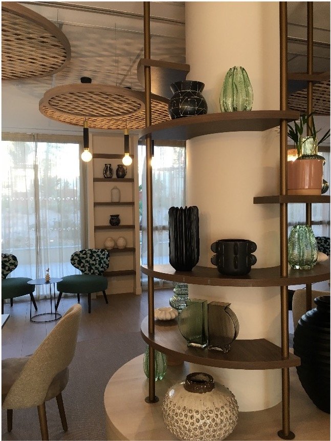 pilier d'intérieur habillé d'étagère sur lequel on voit des objets décoratifs en verre et en céramique et au fond deux fauteils bleu