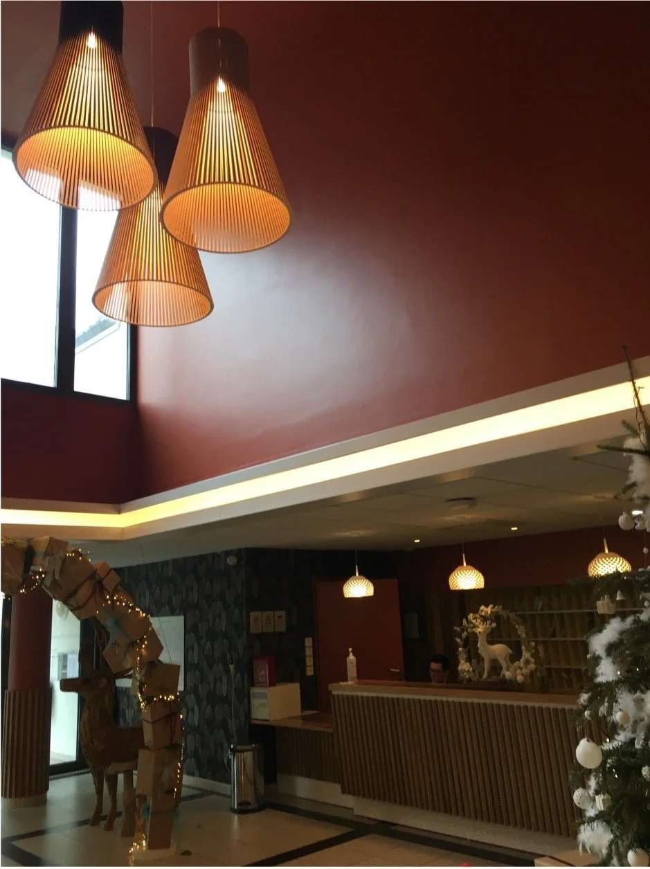 Hall d'accueil avec des murs rouge, des luminaires suspendu au plafond et un comptoir d'accueil