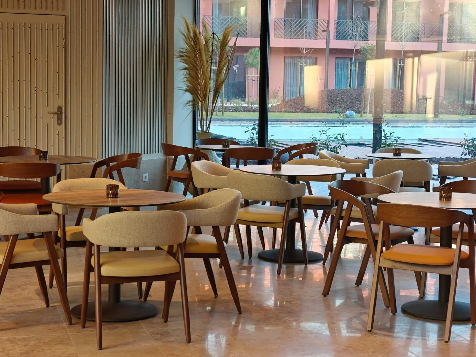 Salle à manger avec des chaises rouge et blanche, des tables en bois et une baie vitrée.