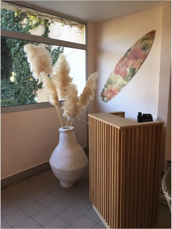 Comptoir d'accueil avec herbes de la pampa dans un vase en papier maché et une planche de surf au mur.