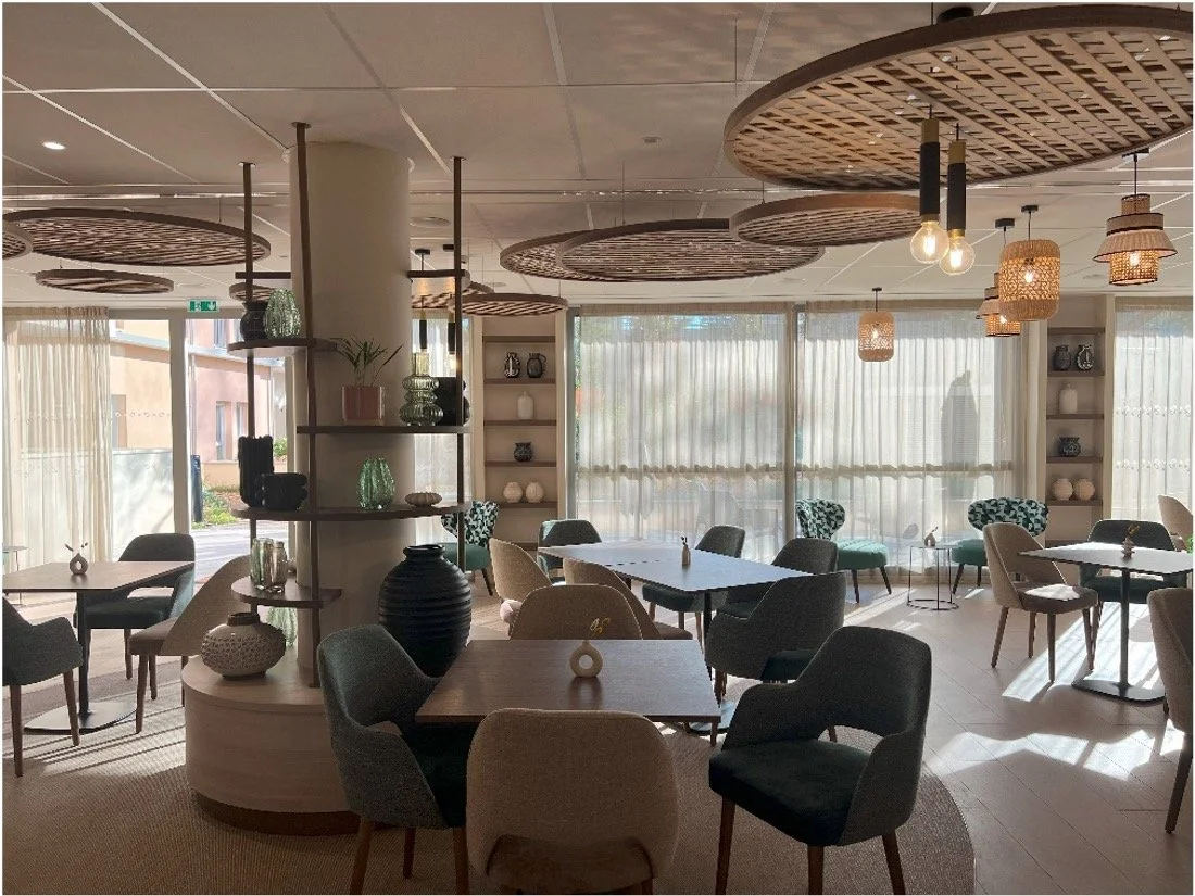 Salle à manger avec des tables en bois, des chaises bleu et blanche. un pilier blanc et des objets décoratifs posé sur des étagère