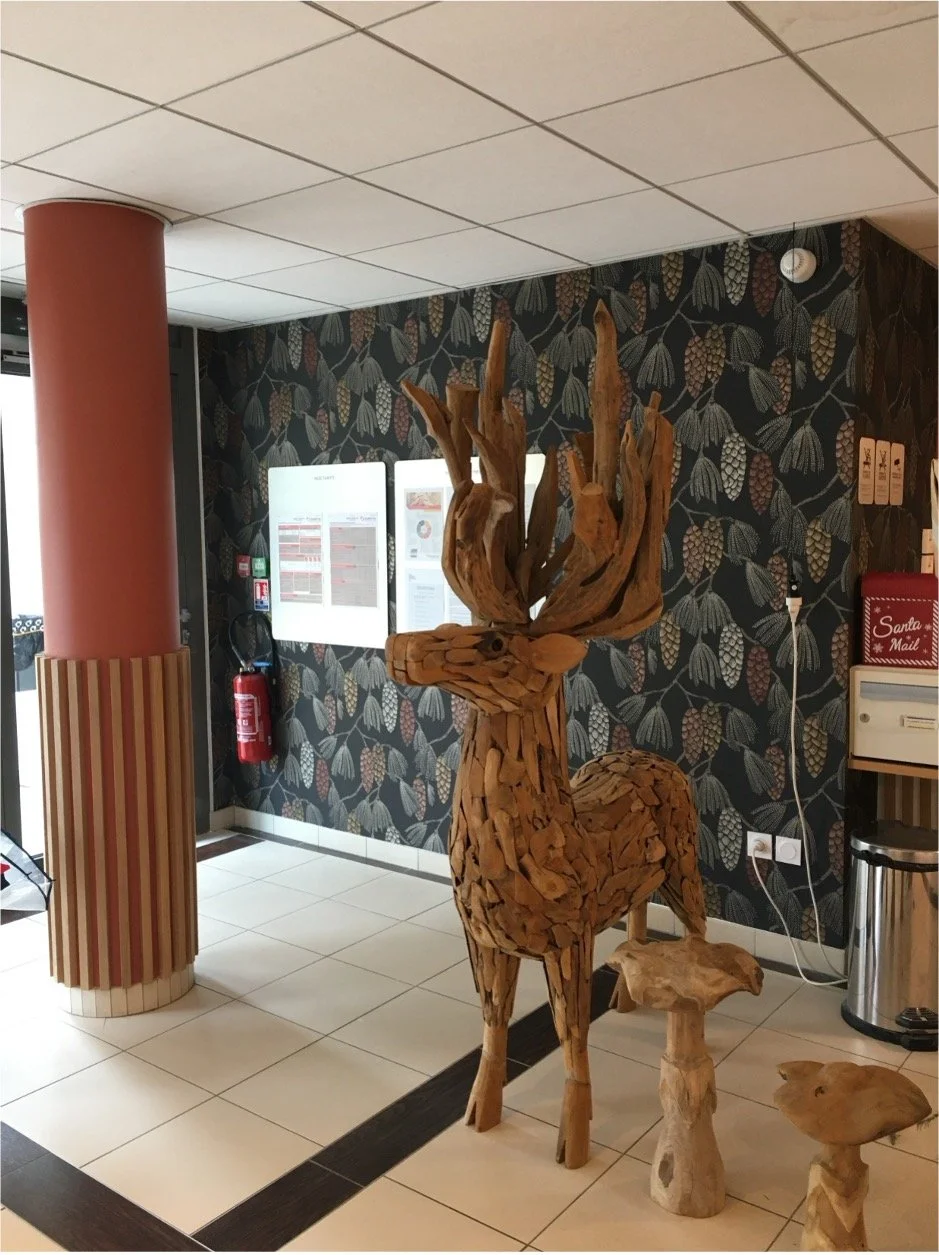 Hall d'accueil avec un pilier rouge, un papier peint illustrant des pommes de pins et un cerf en bois.