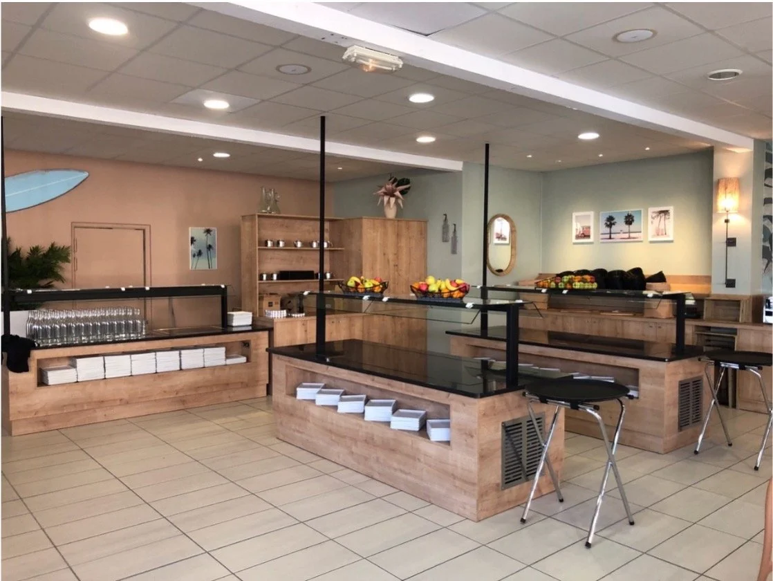 Espace buffet dans un restaurant. Mur vert et terracota avec des tableaux, un miroir et une planche de surf. Etagère en bois.