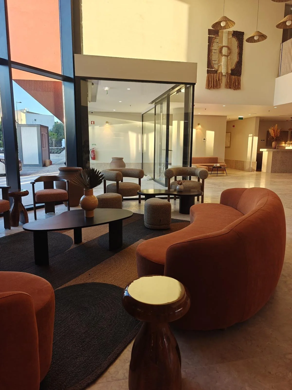 Salle d'accueil avec des tabourets, deux canapé rouge, des luminaires, des tables et des chaises et une baie vitrée.