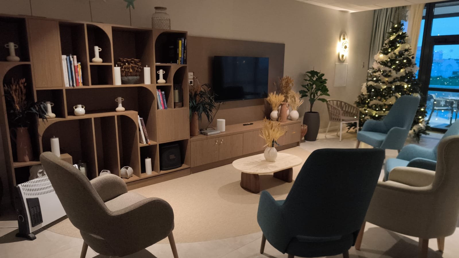 salon avec une bibliothèque avec des livres et décoration dedans. Plusieurs fauteuils bleu et blanc, un sapin de noël, une telévision et une table basse en bois et en marbre.