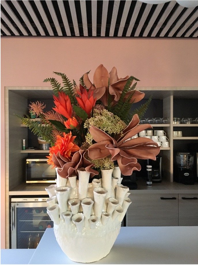 Bouquet de fleur orange et rose saumon dans un vase en forme de corail posé sur un comptoir