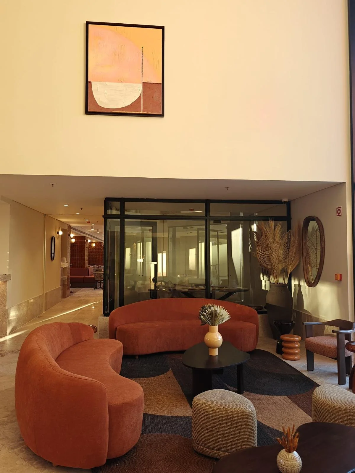 Salon avec deux canapé rouge, une table noir, des tabourets gris, un tableau graphique, des pots de fleur et une baie vitrée