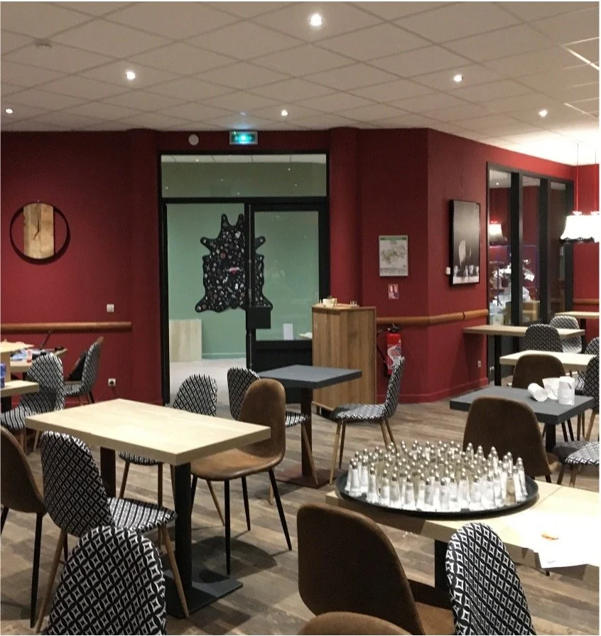 Restaurant avec chaise et table avec un mur bordeaux et une double porte vitré. Decoration murale avec une peau de vache