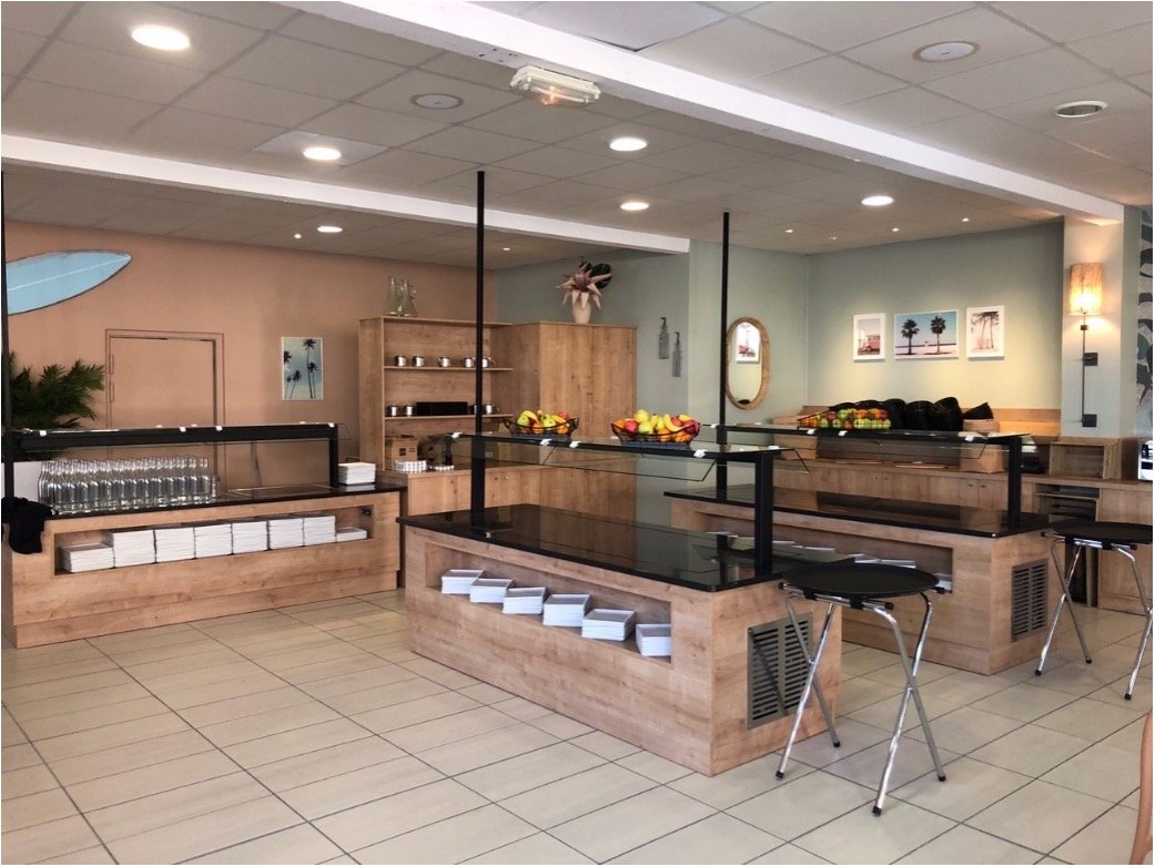 Espace buffet dans un restaurant. Mur vert et terracota avec des tableaux, un miroir et une planche de surf. Etagère en bois.