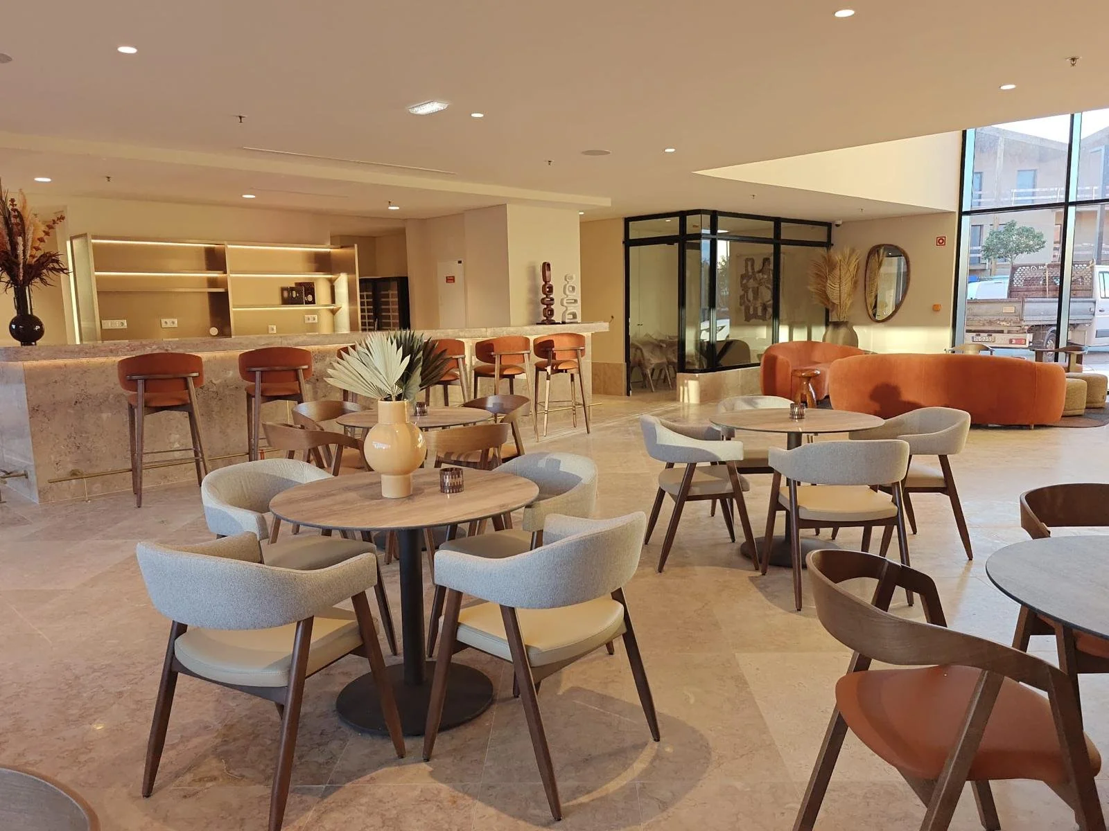 Salle avec deux canapé rouge, des chaises blanche et rouge, des table en bois, des pots de fleur, des chaises hautes rouges et un comptoir de bar.