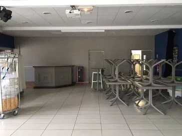 Salle de buffet avec des chaises blanches rangées l'une sur l'autre. Un mur blanc et bleu avec deux portes au fond.