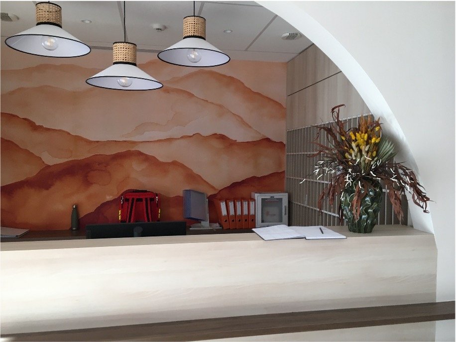 Comptoir d'accueil avec un papier peint rouge, des luminaires suspendu et un bouquet de fleur jaune et vert dans un vase