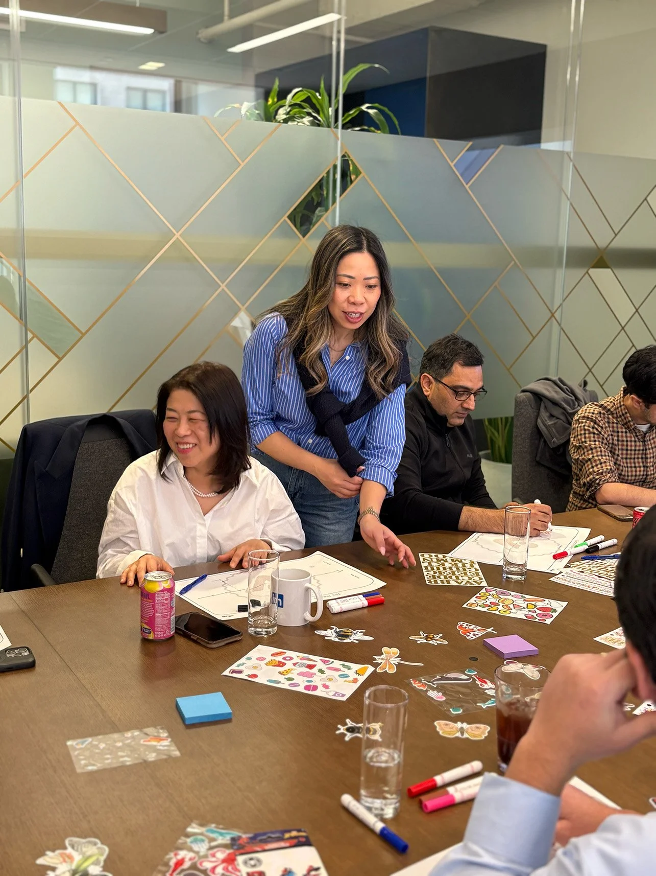 Group of people in an office meeting room with markers, paper, and drinks on the table, engaged in a discussion.
