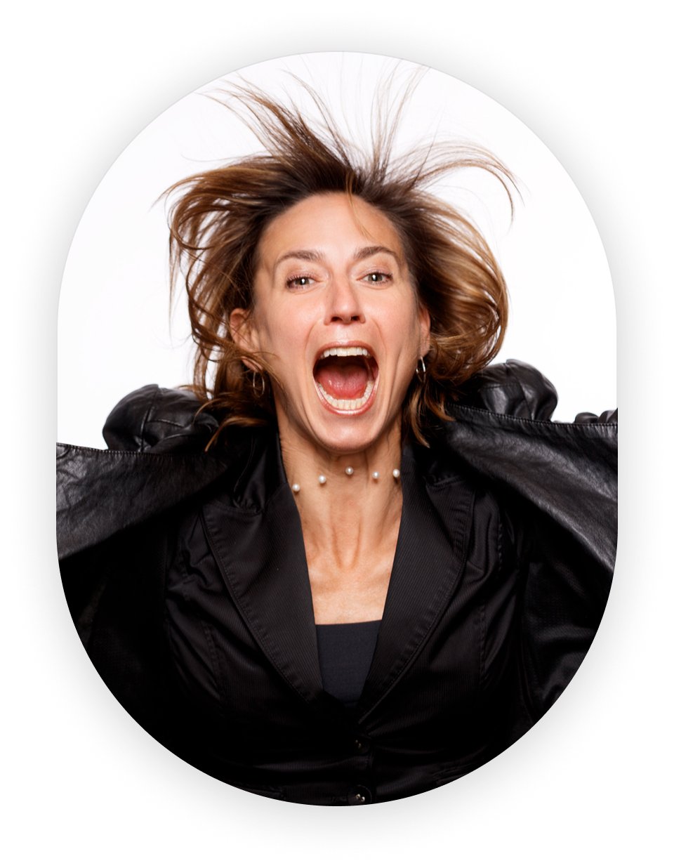 A woman with curly brown hair, wearing a black jacket and pearl necklace, screams with her mouth open and hair flying up.